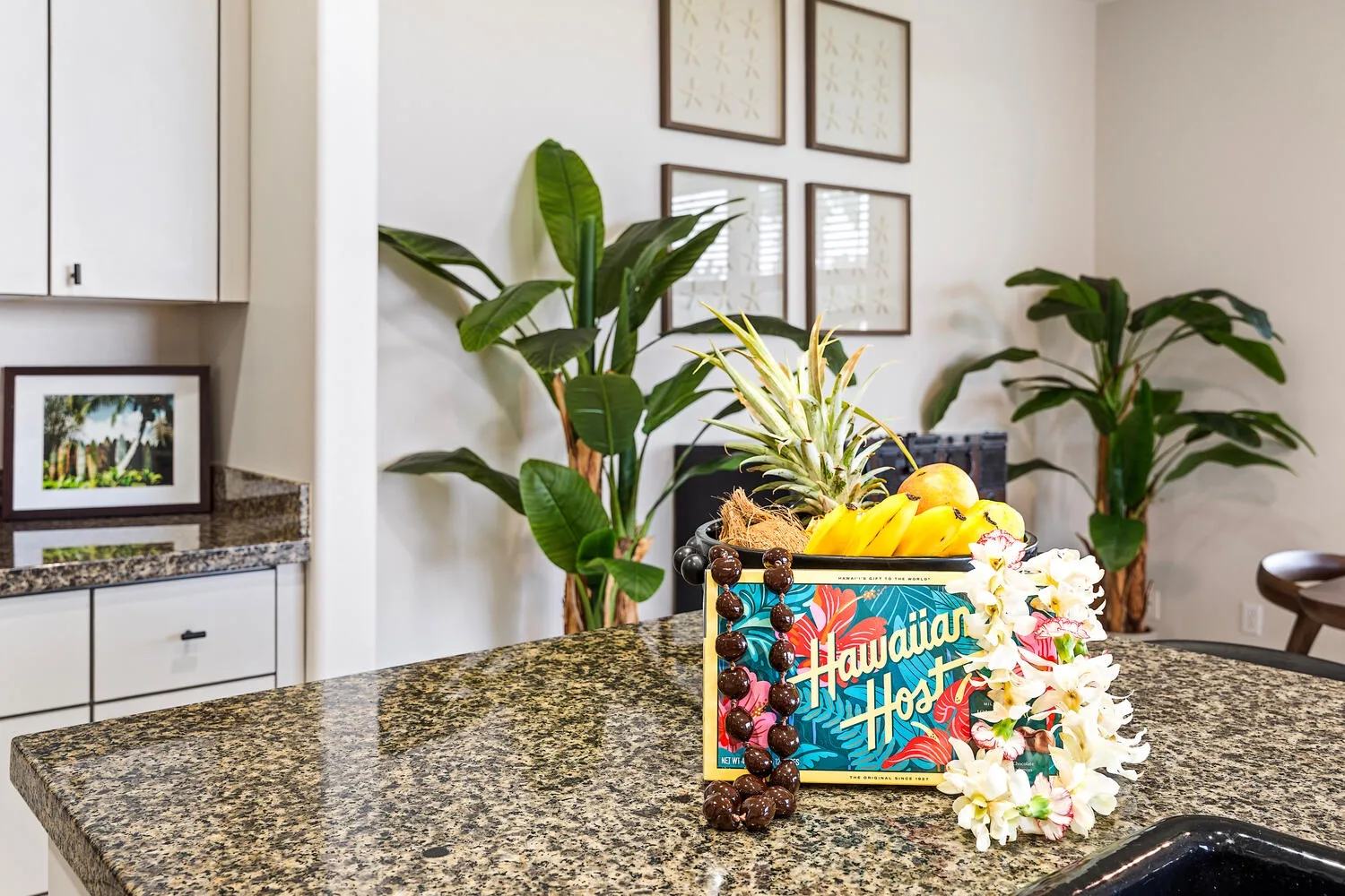 A bright kitchen counter displays a colorful fruit box and tropical flowers.