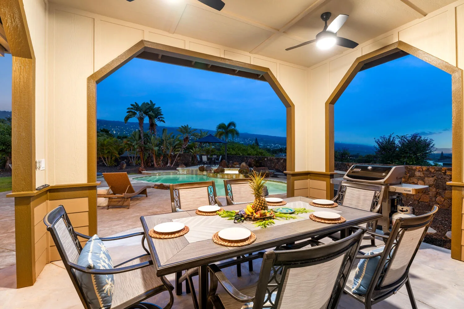 A covered outdoor dining area overlooks a pool and tropical landscape.