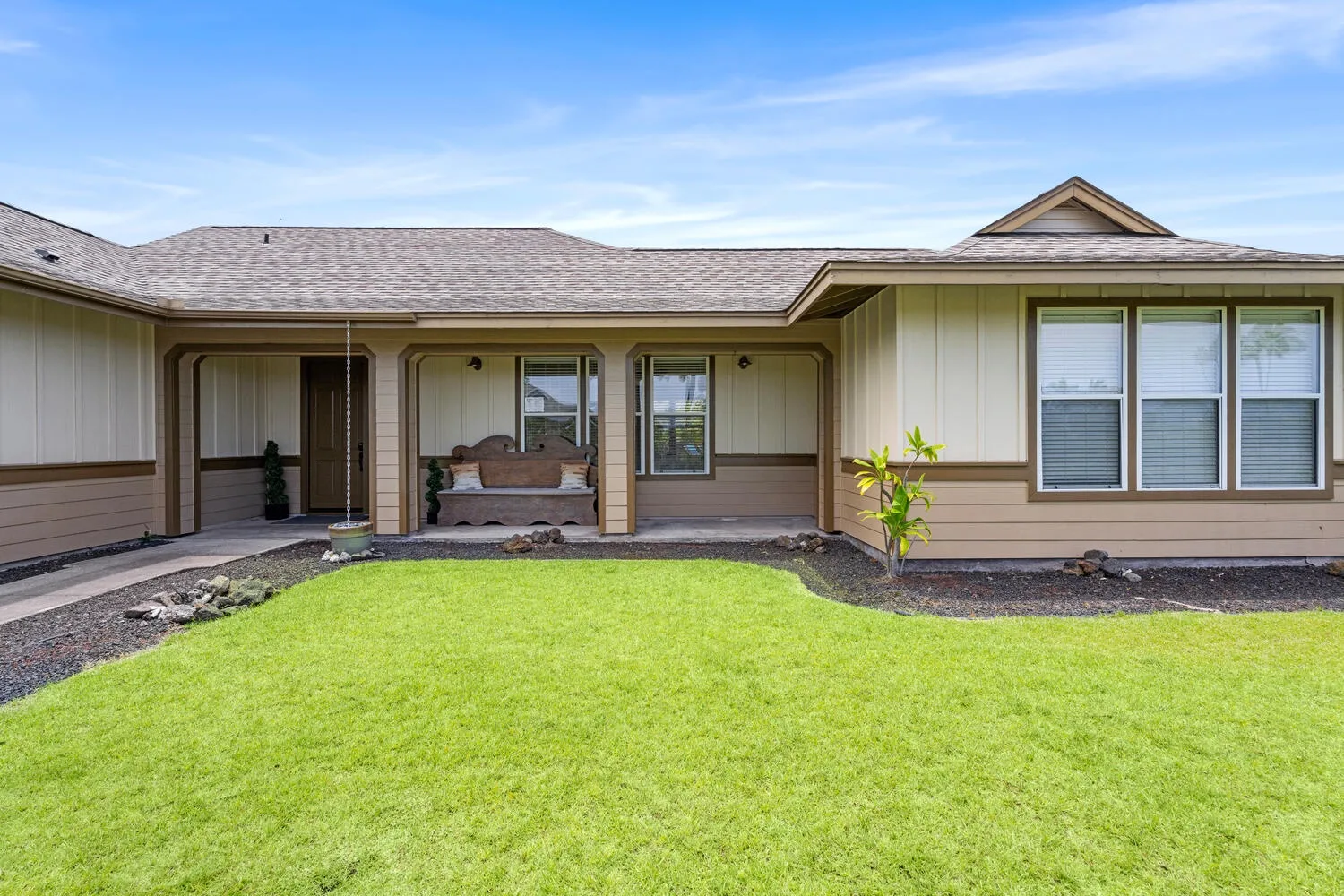 A single-story house faces a green lawn, with a covered patio and large windows.