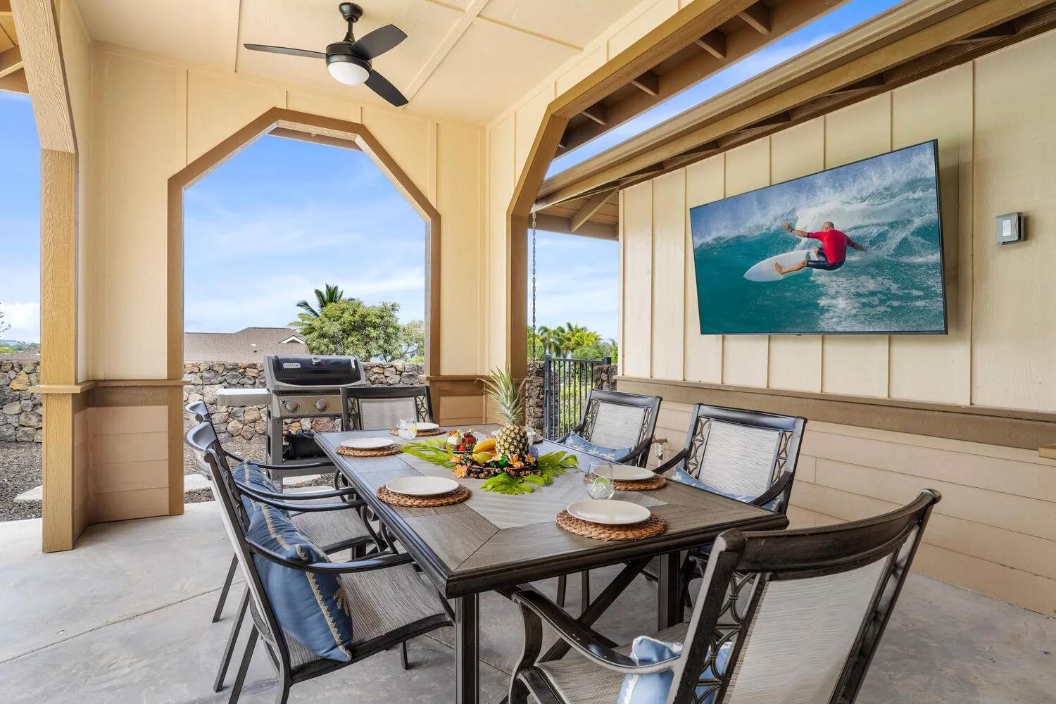 A covered outdoor dining area with a set table and a wall-mounted screen.