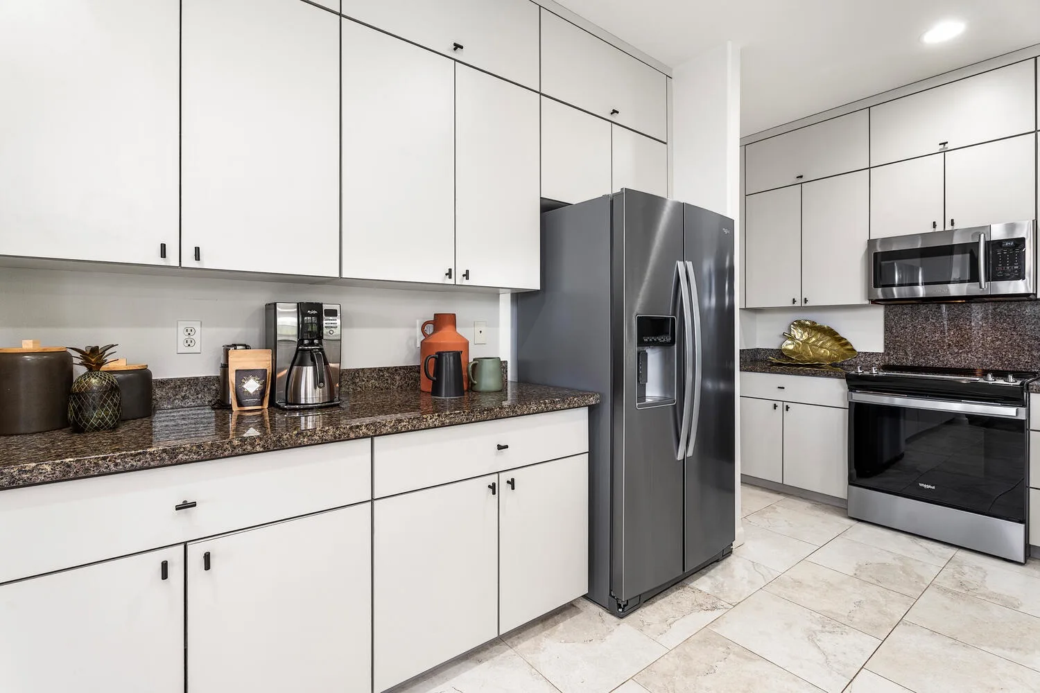 A bright kitchen with white cabinets and dark countertops.