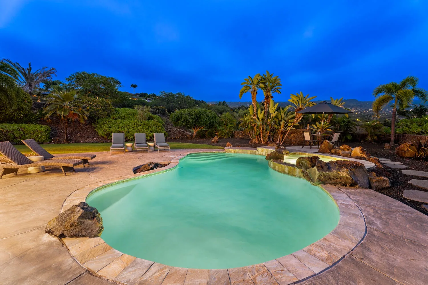 A curved outdoor swimming pool is surrounded by stone paving and lounge seating.
