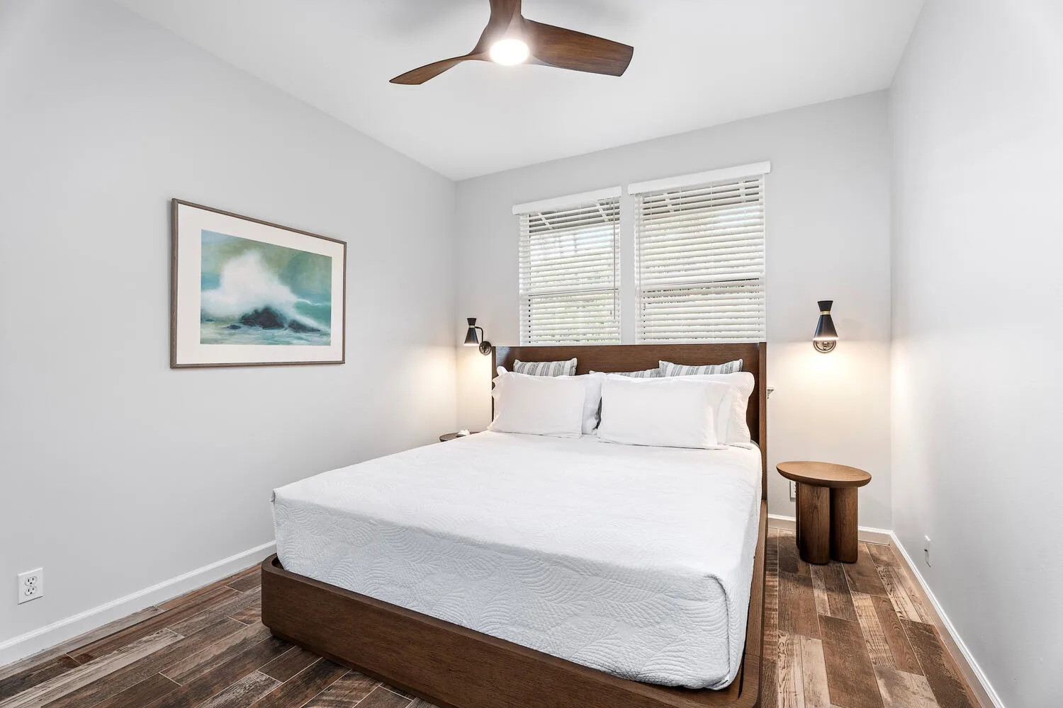 A bright bedroom with a neatly made bed beneath two windows.