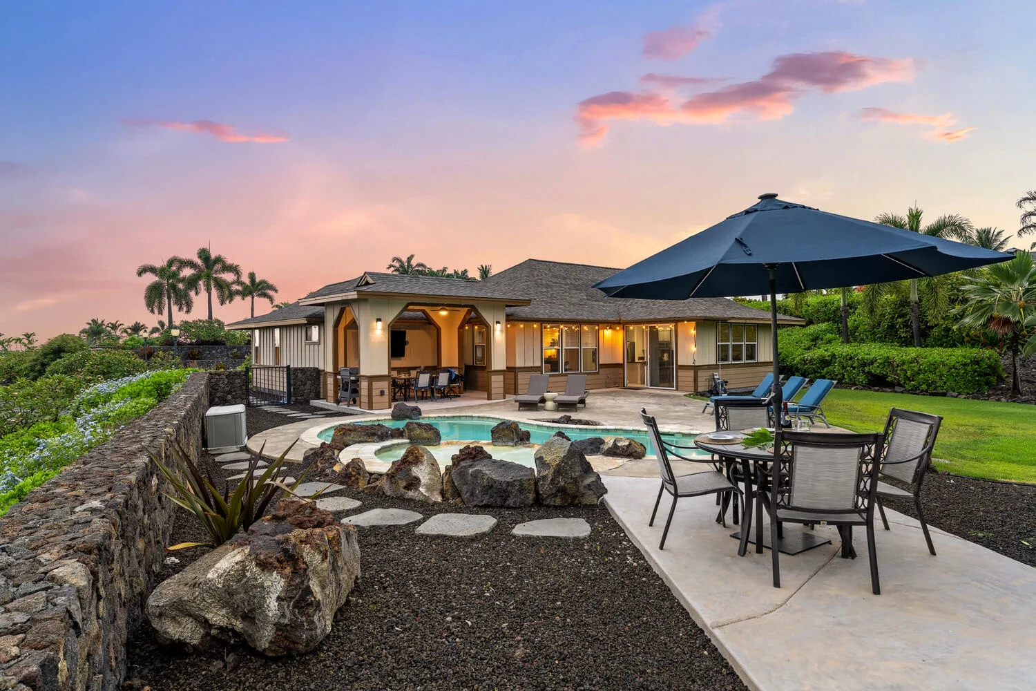 A landscaped outdoor pool and patio sit beside a single-story house at sunset.
