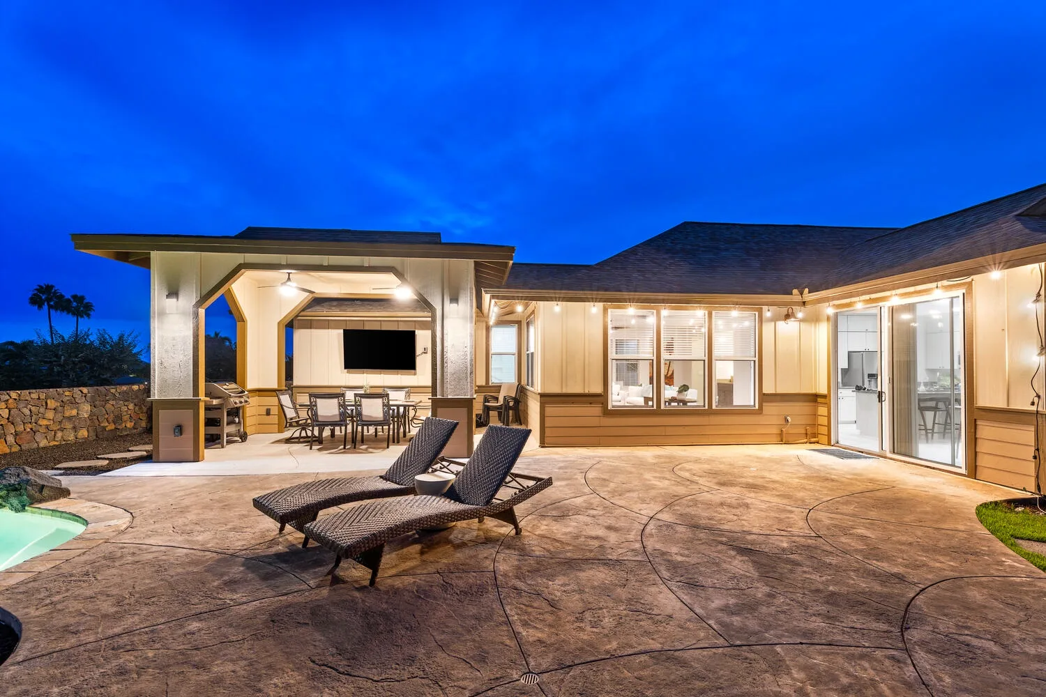 A spacious outdoor patio with lounge seating, a dining area, and a pool edge.