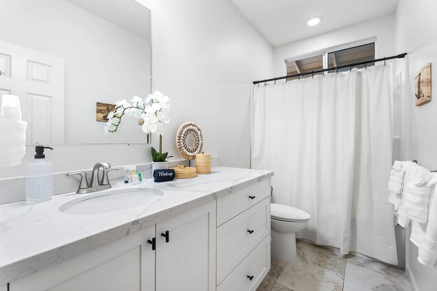 A bright bathroom has a long vanity beside a curtained shower.