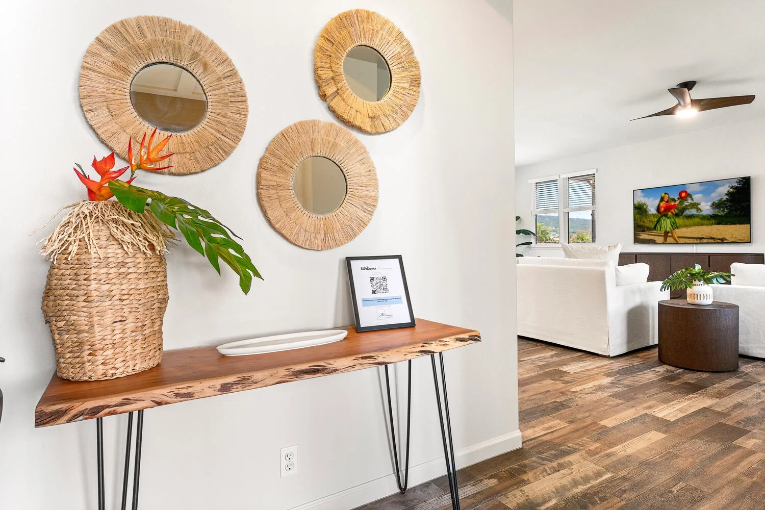 A bright living room with a white sofa, coffee table, and wall-mounted television.