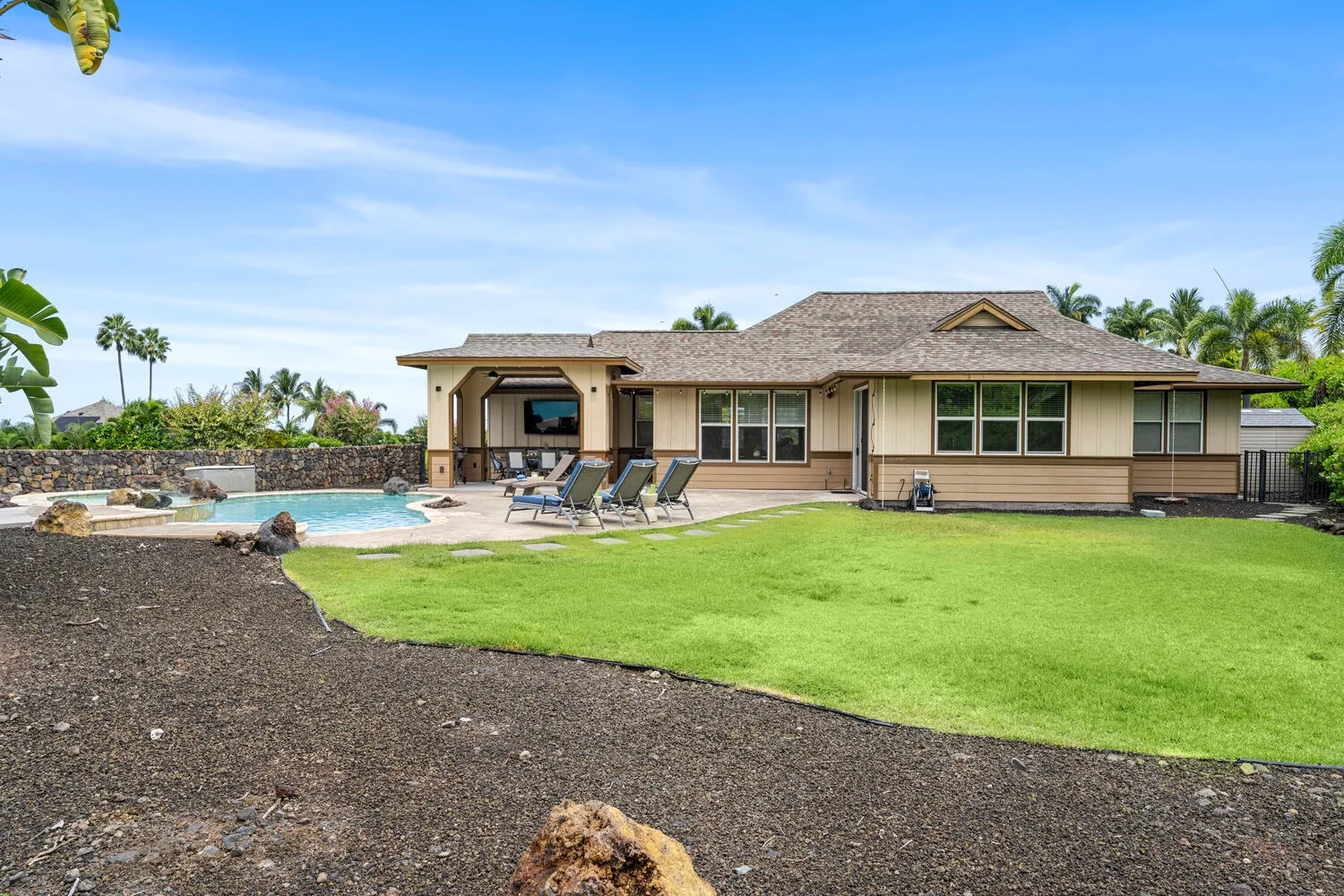 A single-story house beside a lawn, with a swimming pool and outdoor seating.