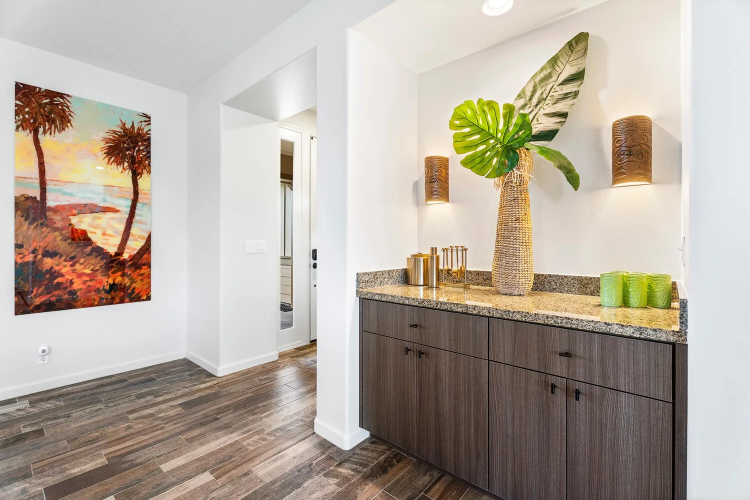 A hallway with a dark wood cabinet, decorative plants, and colorful wall art.