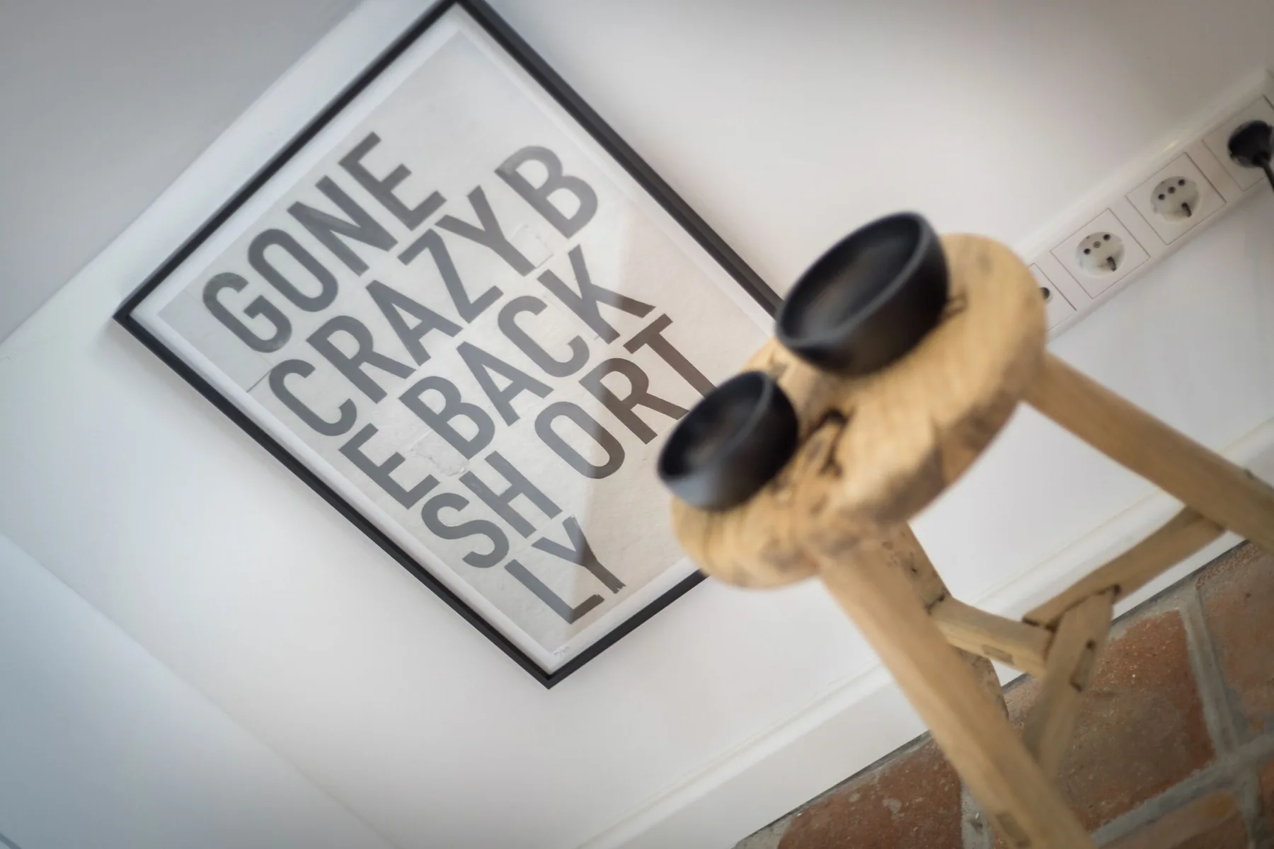 A framed typographic poster hangs on a white wall above a wooden railing.