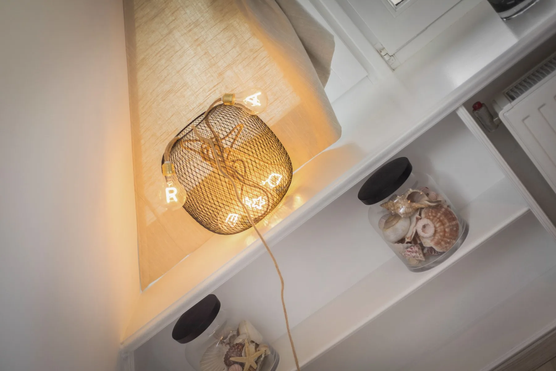 A woven pendant lamp hangs above white shelving with decorative bowls.