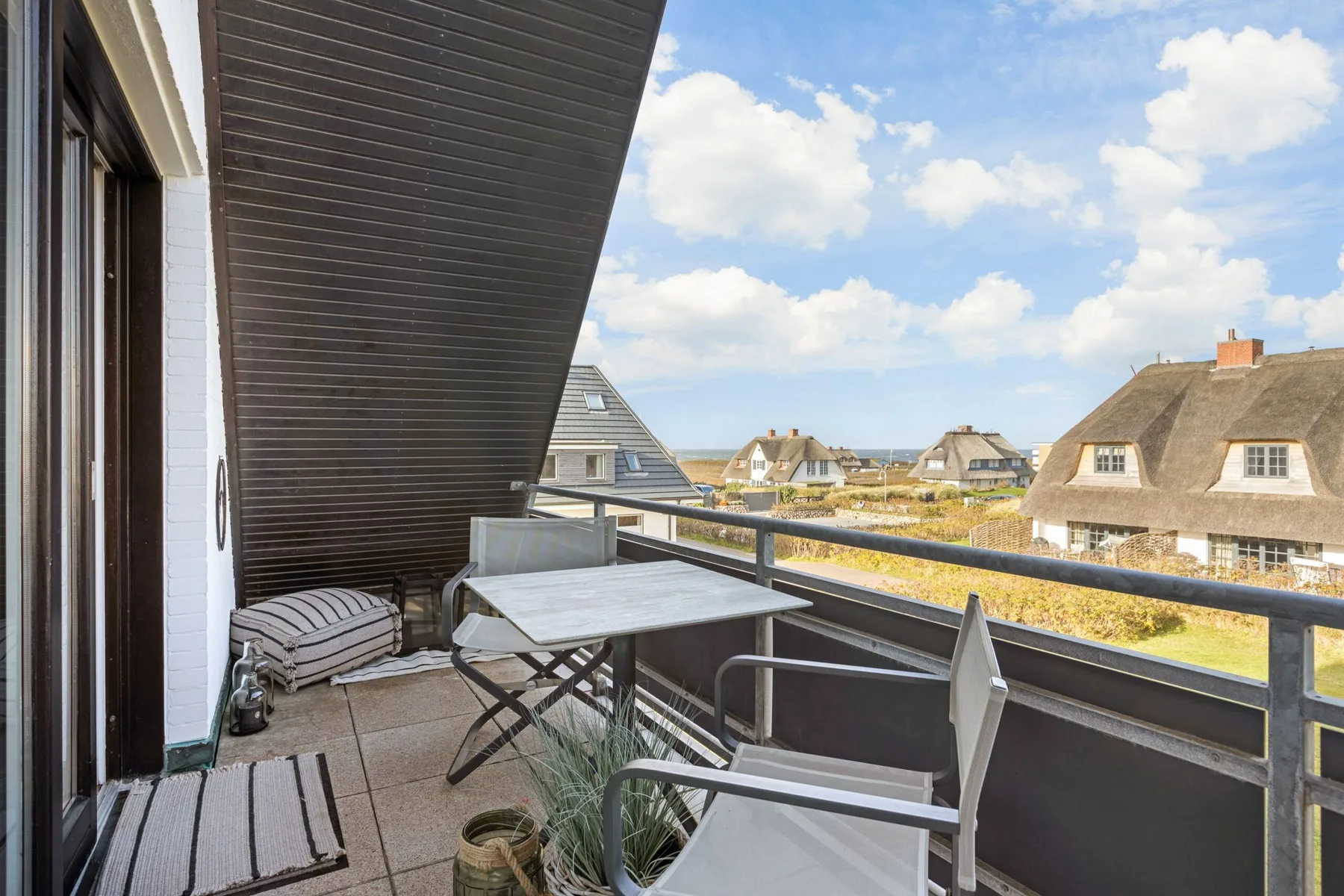 A balcony with outdoor seating overlooks nearby houses and greenery.
