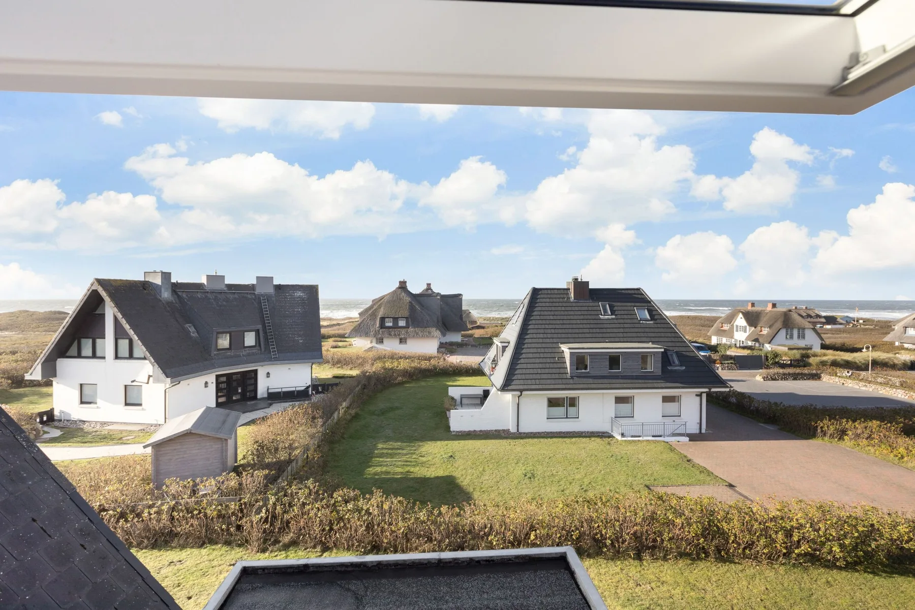 Detached houses stand among grassy yards beneath a partly cloudy sky.