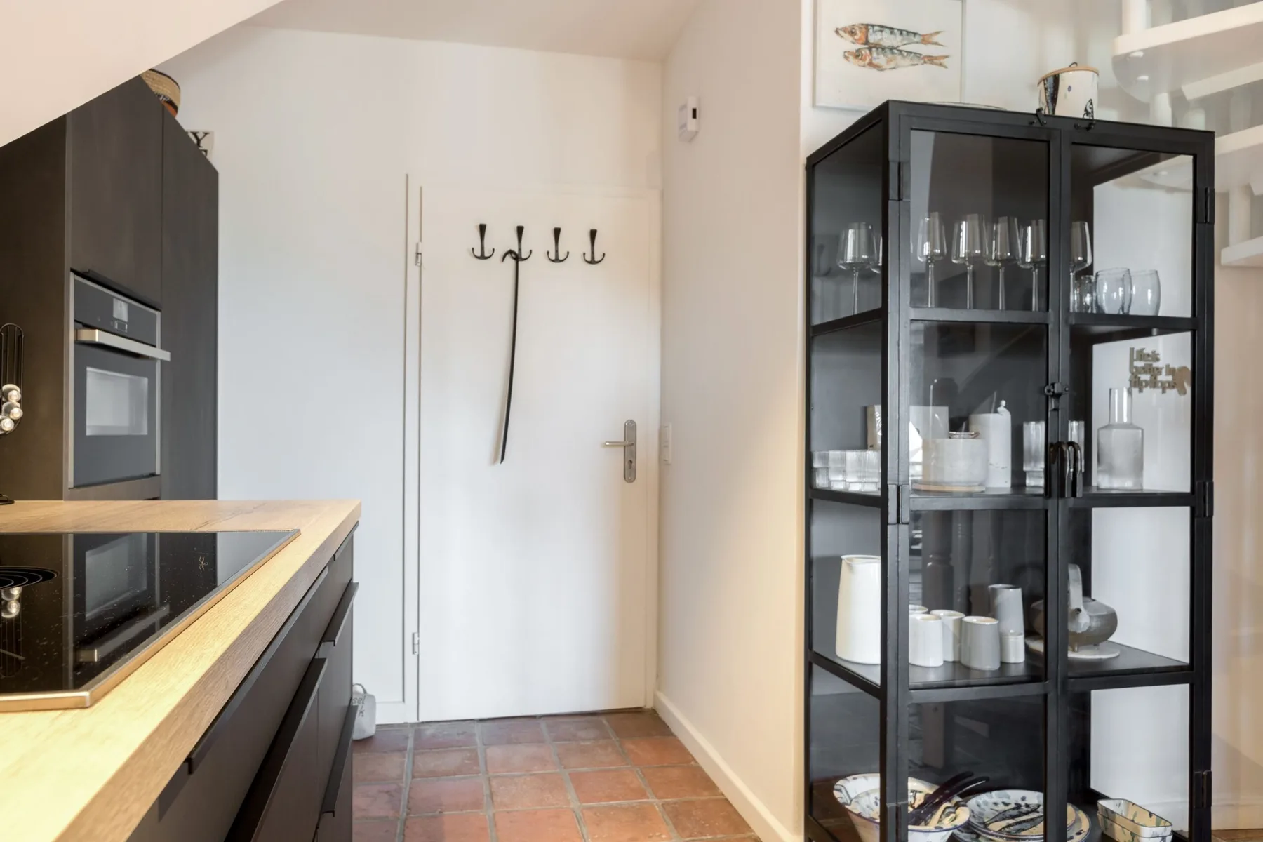 A kitchen with dark cabinetry, a cooktop, and a glass-front display cabinet.
