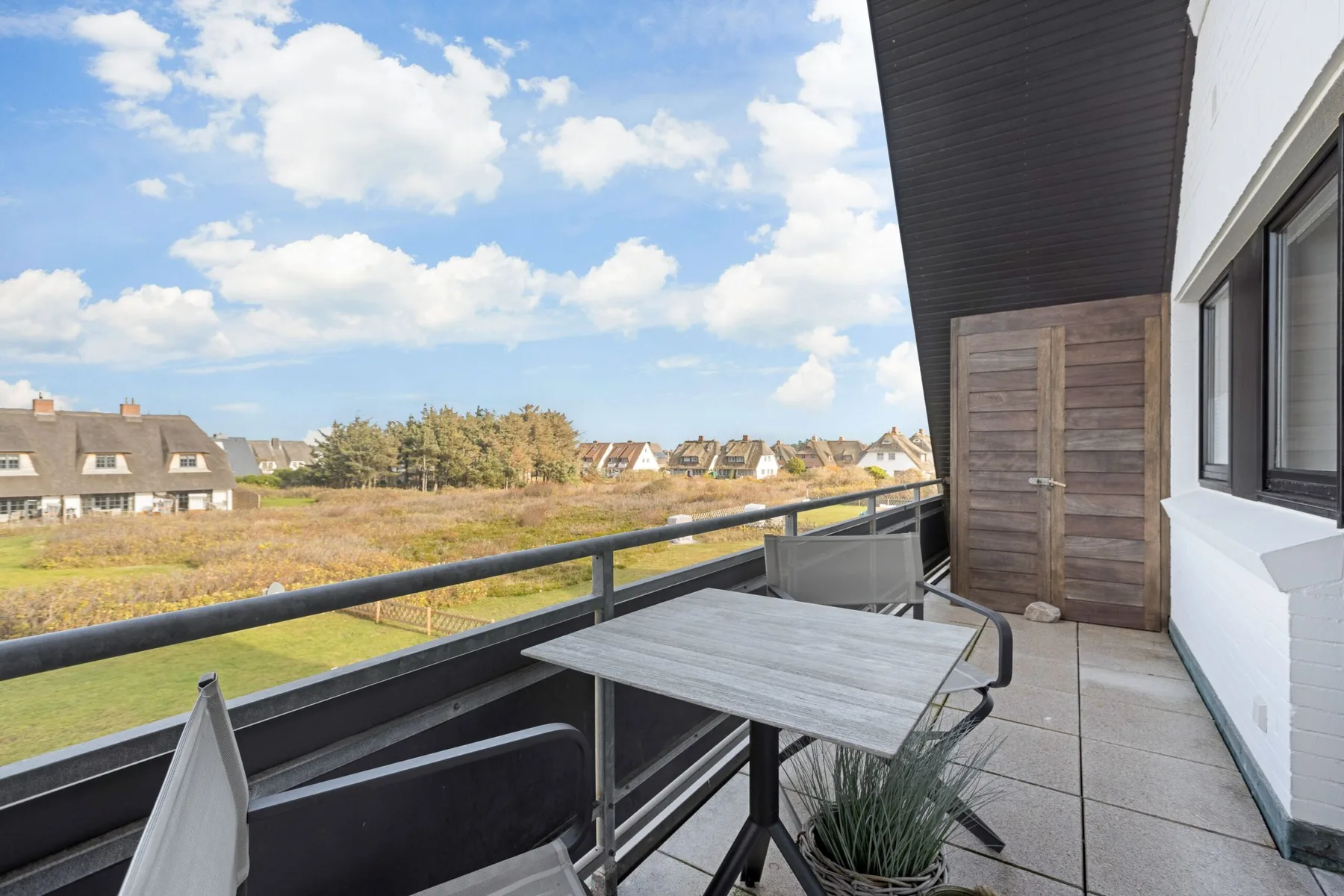 A balcony with outdoor seating overlooks open fields and nearby houses.