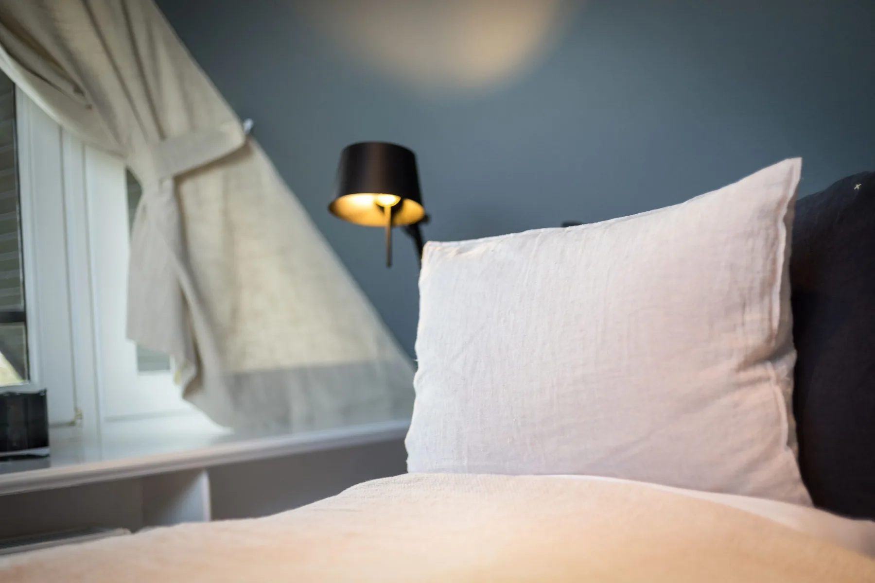 A bedroom scene shows a bed beside a window with a tied-back curtain.