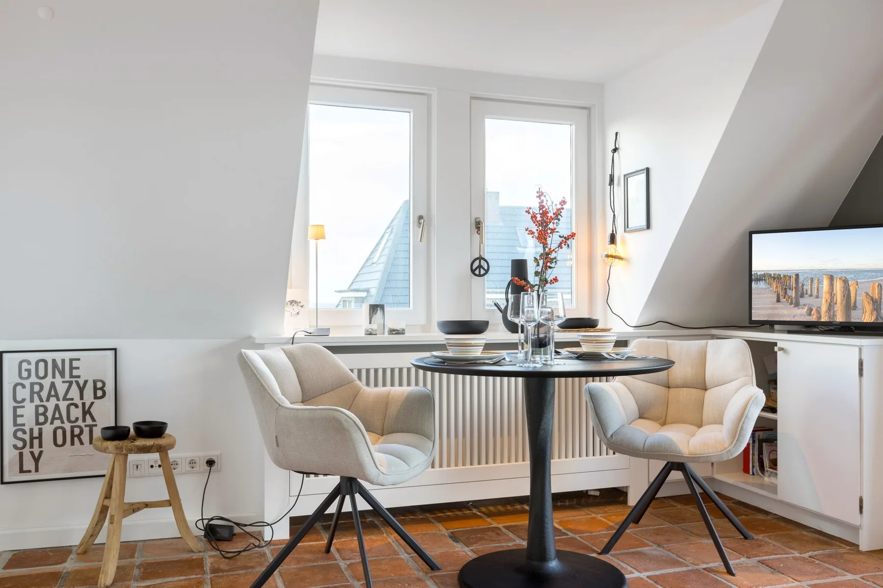 A bright dining area with a round table and upholstered seating beside tall windows.