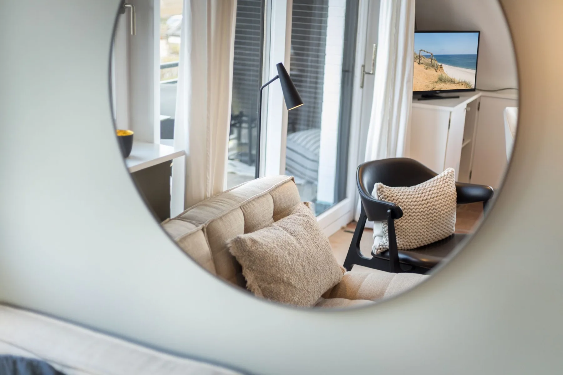 A sitting area with a sofa, armchair, and floor lamp beside glass doors.