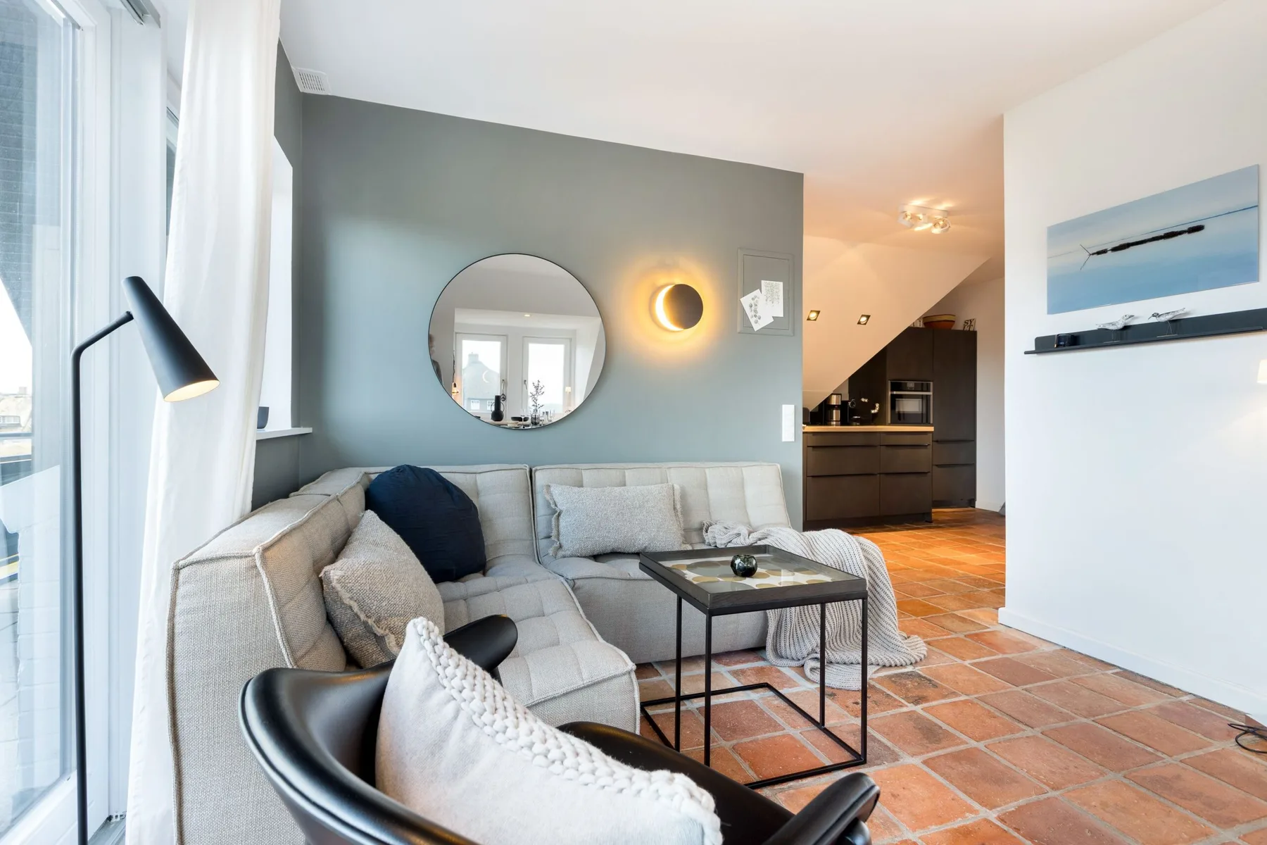 A living room with seating and a coffee table, opening onto a kitchen.