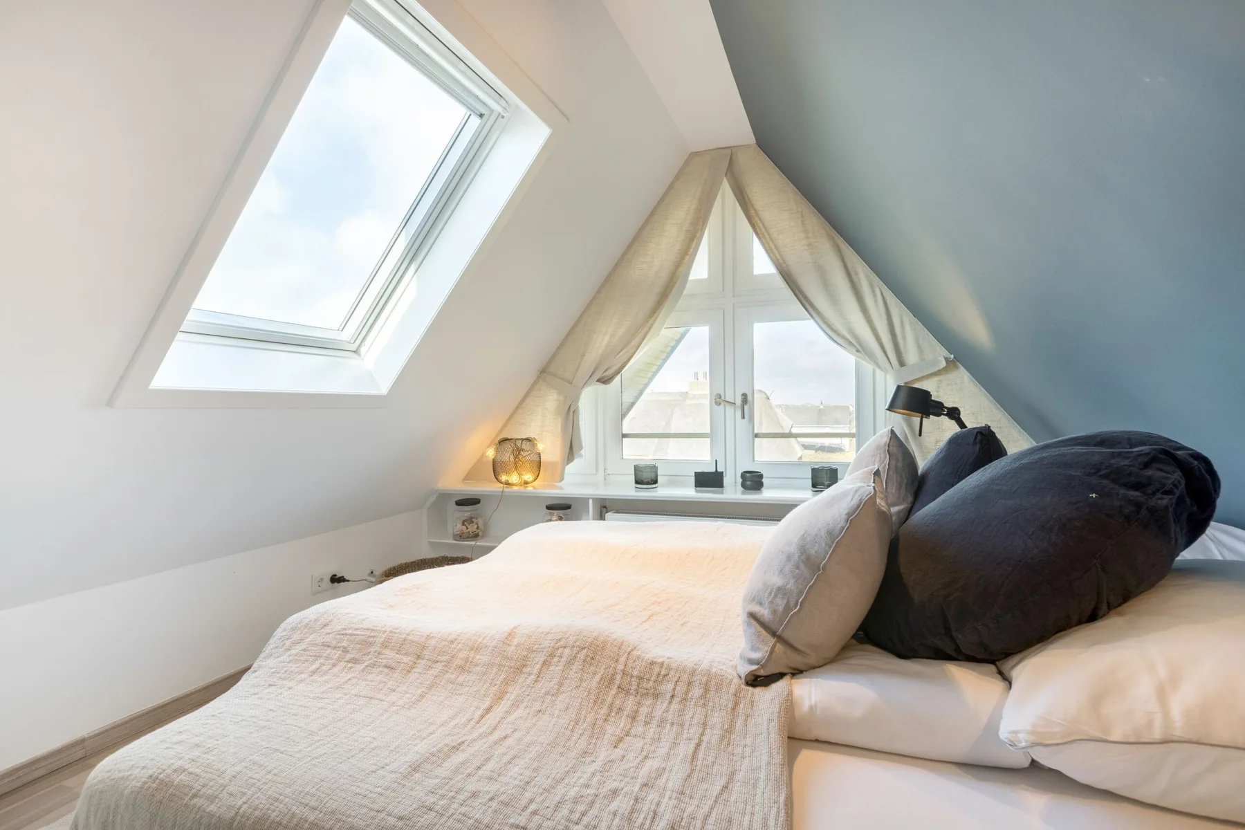 A bright attic bedroom with a bed beneath sloped ceilings and a skylight.