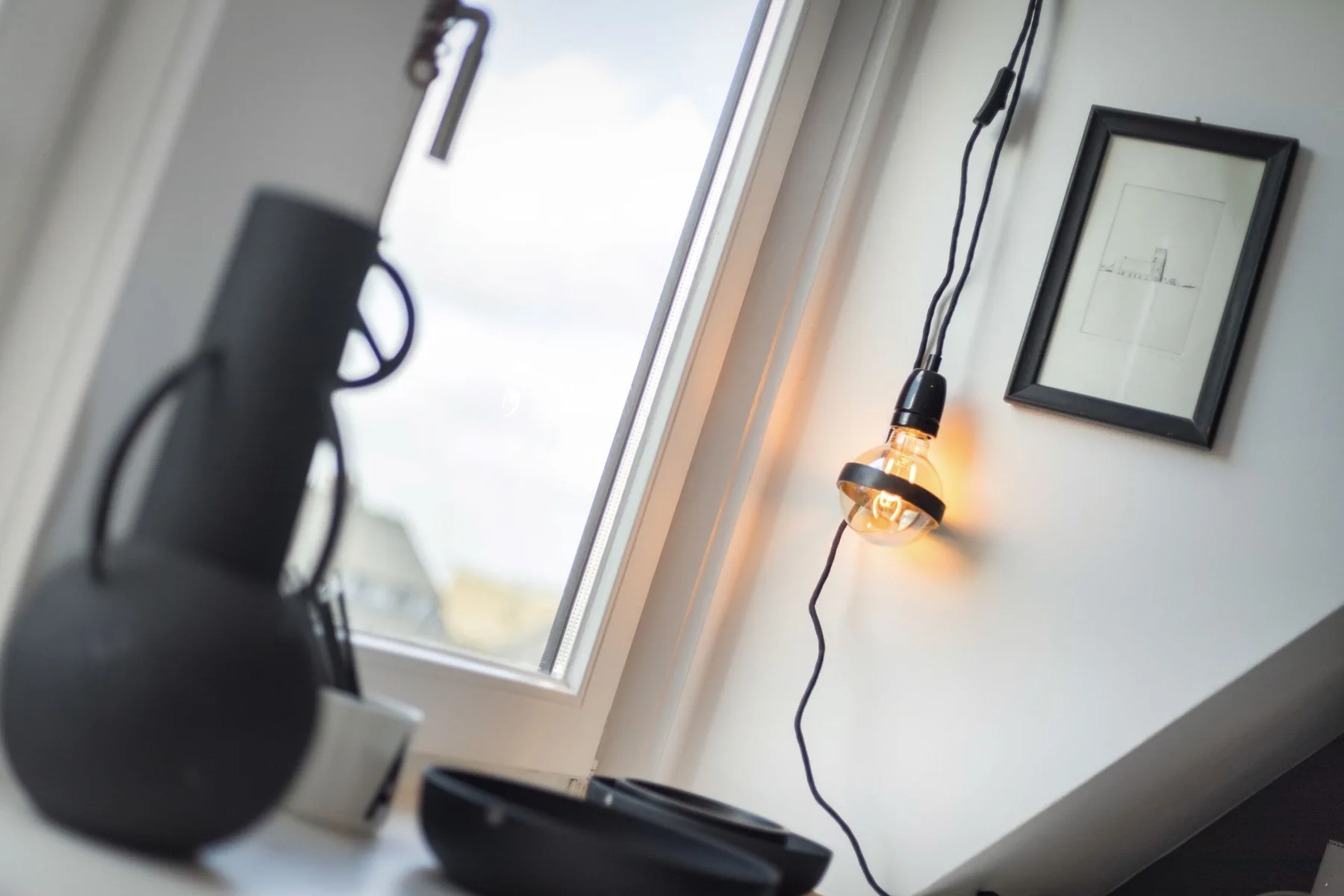 A bright room corner with a large window, hanging lamp, and framed picture.