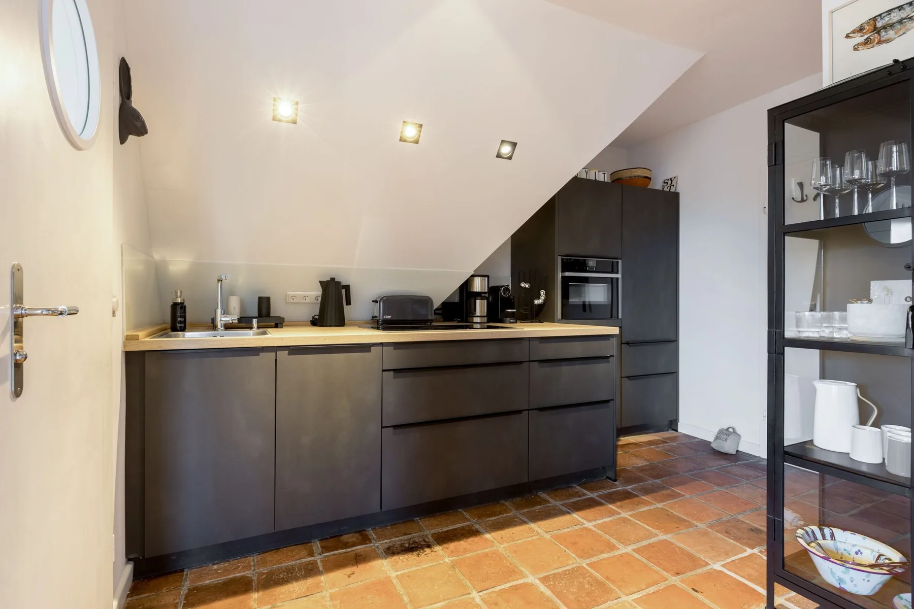 A compact kitchen with dark cabinets, a countertop, and terracotta-colored floor tiles.