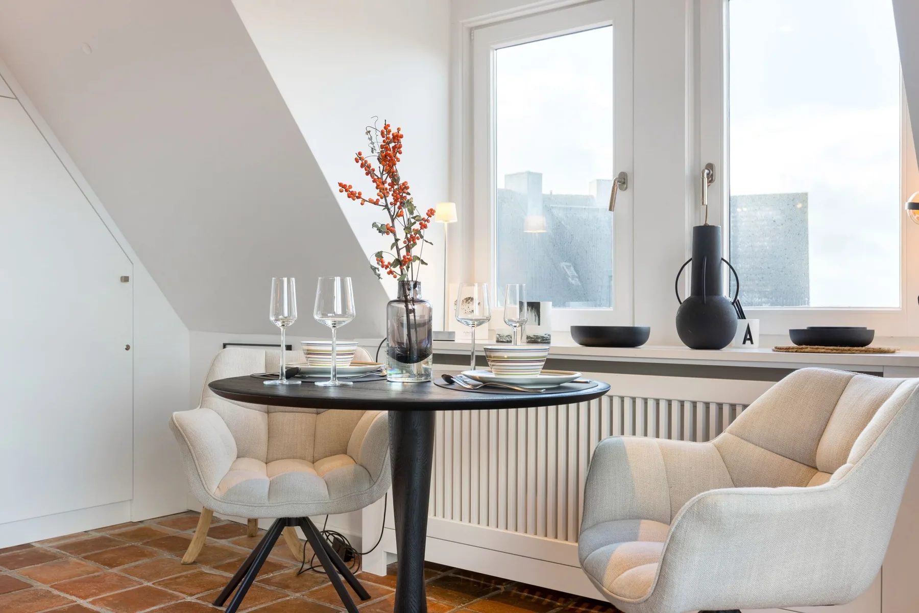 A dining table with upholstered seating sits beside large windows in a bright room.