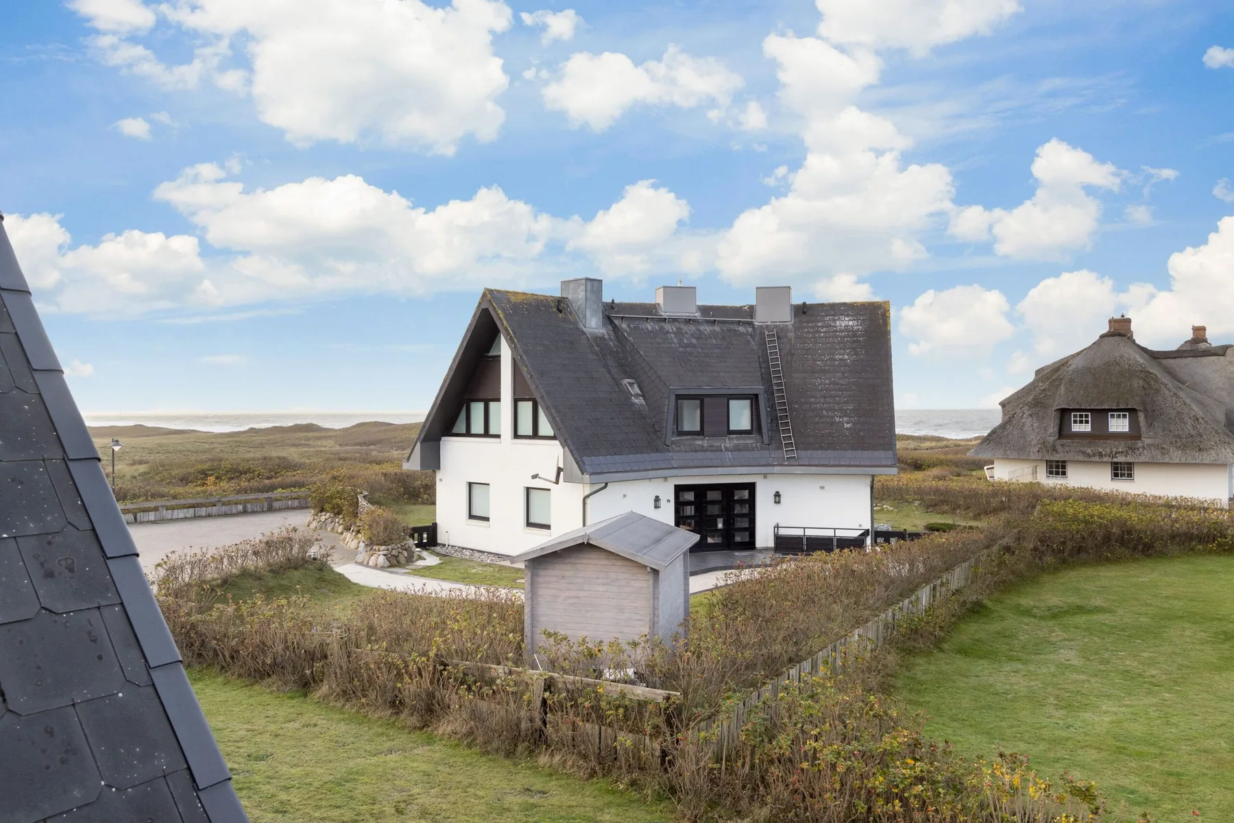 A white house with a dark roof stands in an open grassy landscape.