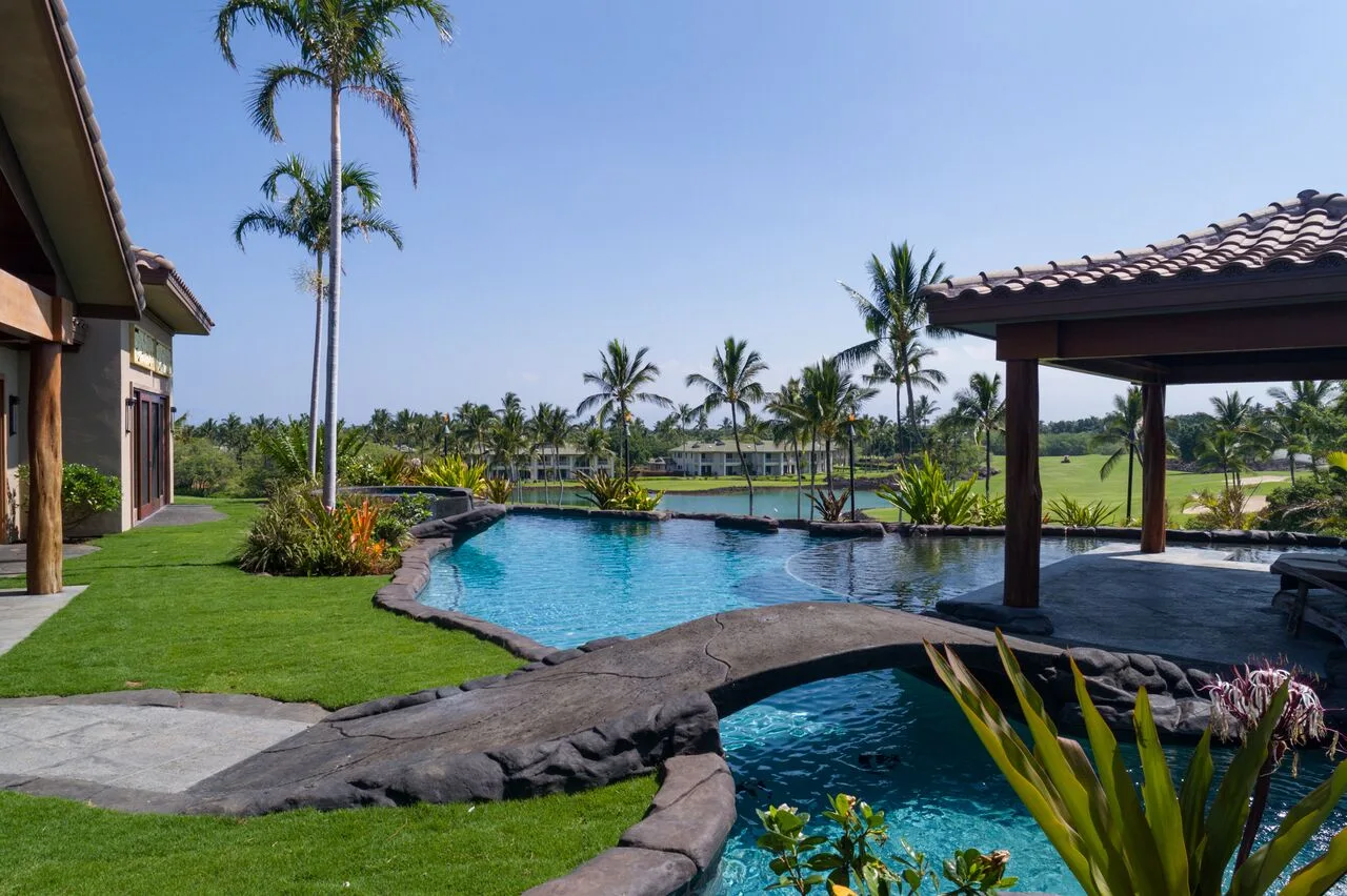 Zona de piscina al aire libre con una pérgola cubierta y vegetación tropical.