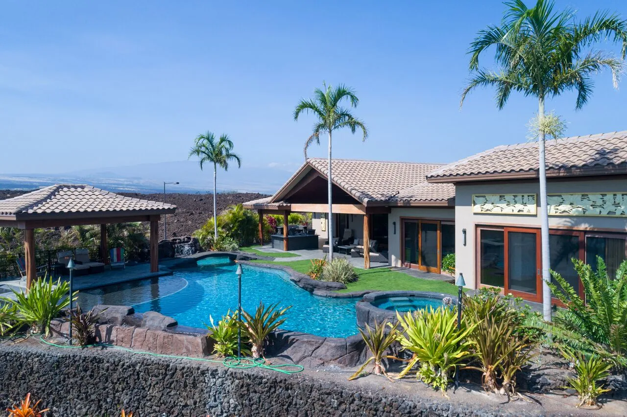 Una casa moderna y una piscina están rodeadas de plantas tropicales y palmeras.