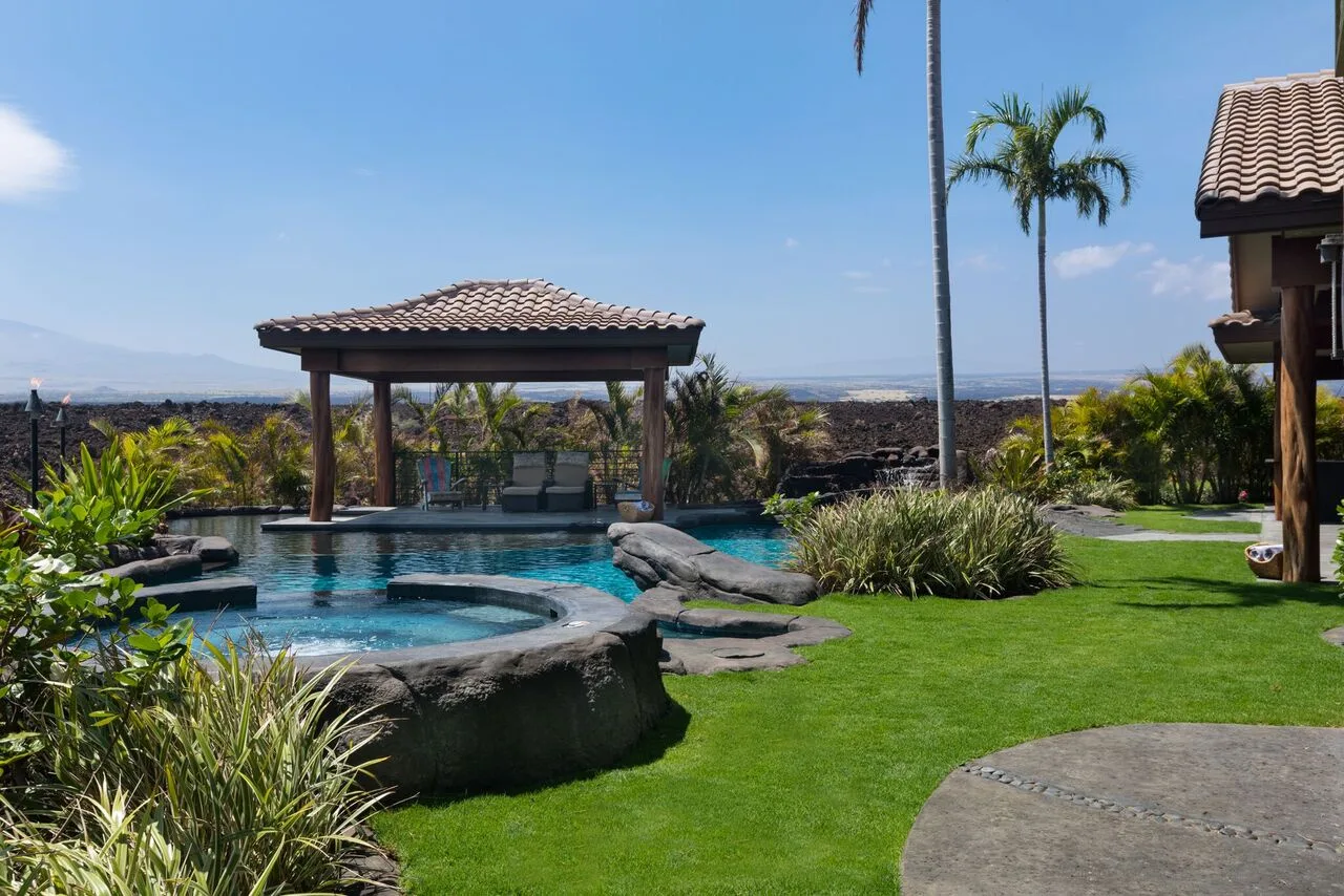 Una piscina al aire libre junto a un pabellón cubierto, rodeada de vegetación.