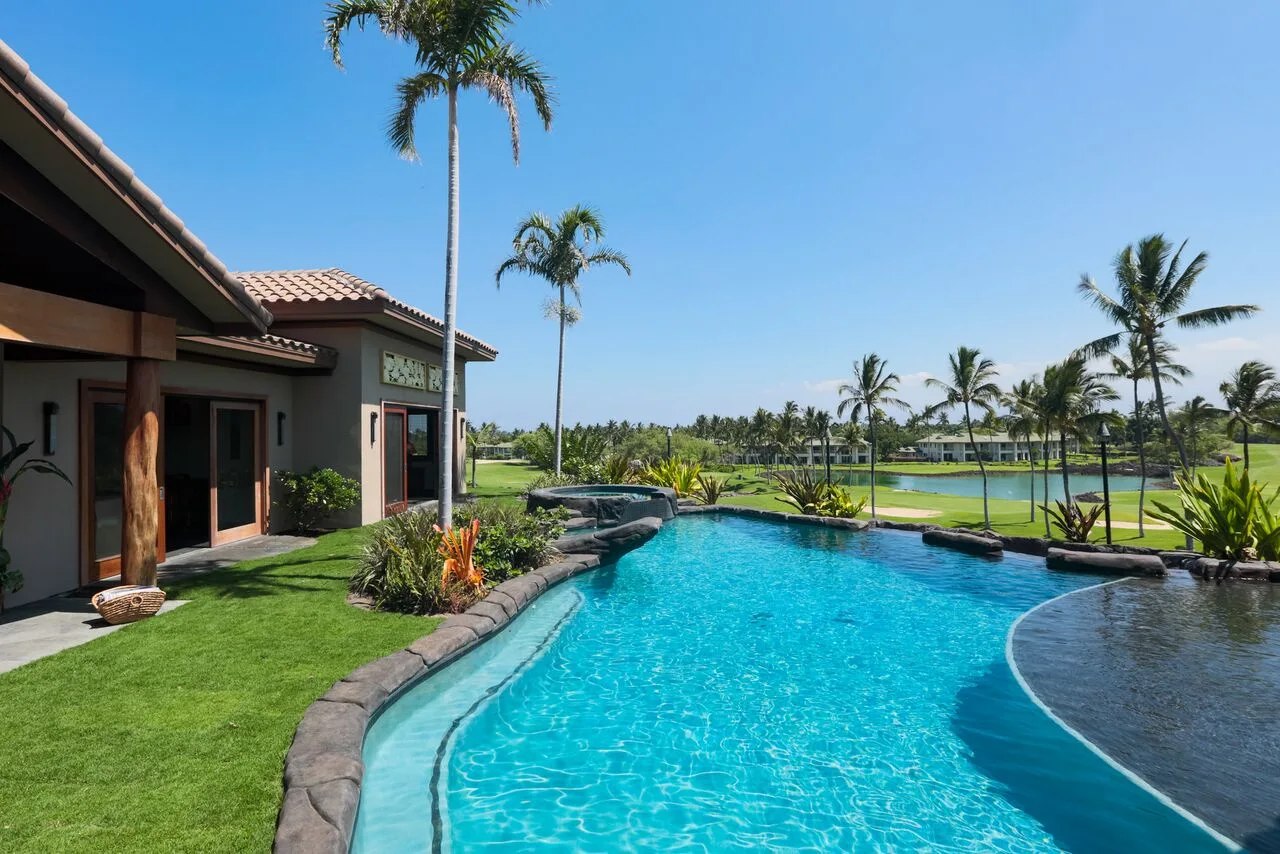 Una piscina exterior curva junto a un césped ajardinado y palmeras.