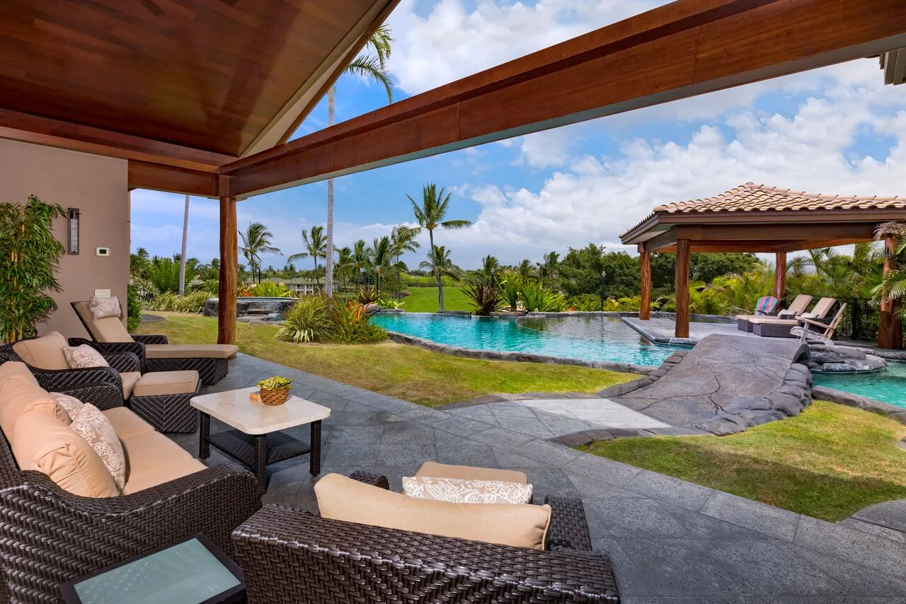 Un patio exterior con asientos acolchados da a una piscina y un jardín.