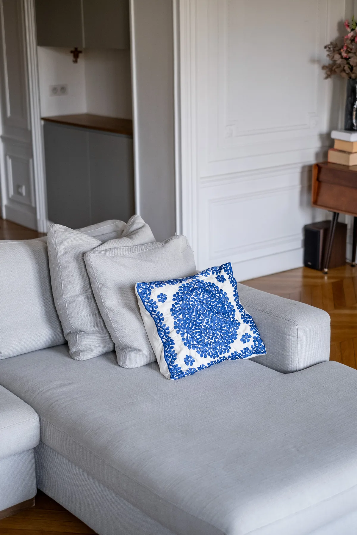 Un sofá claro con un cojín estampado azul está en una sala de estar.
