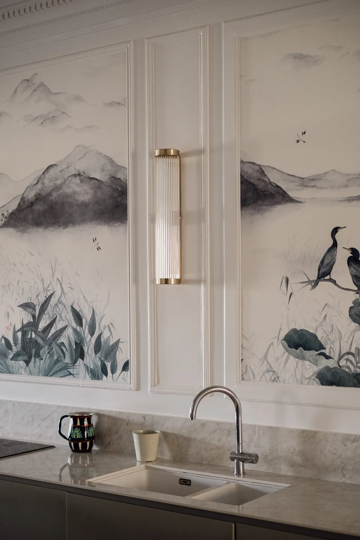 Un lavabo de baño está bajo paneles decorativos con paisajes.