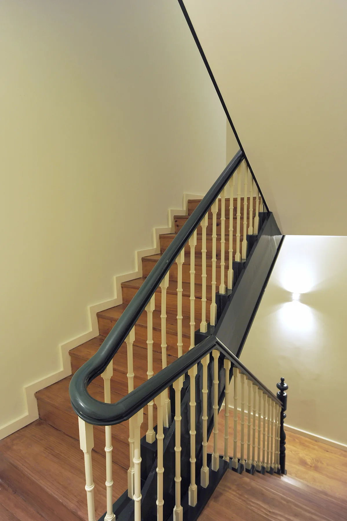 Una escalera de madera con barandales oscuros sube junto a una pared clara.