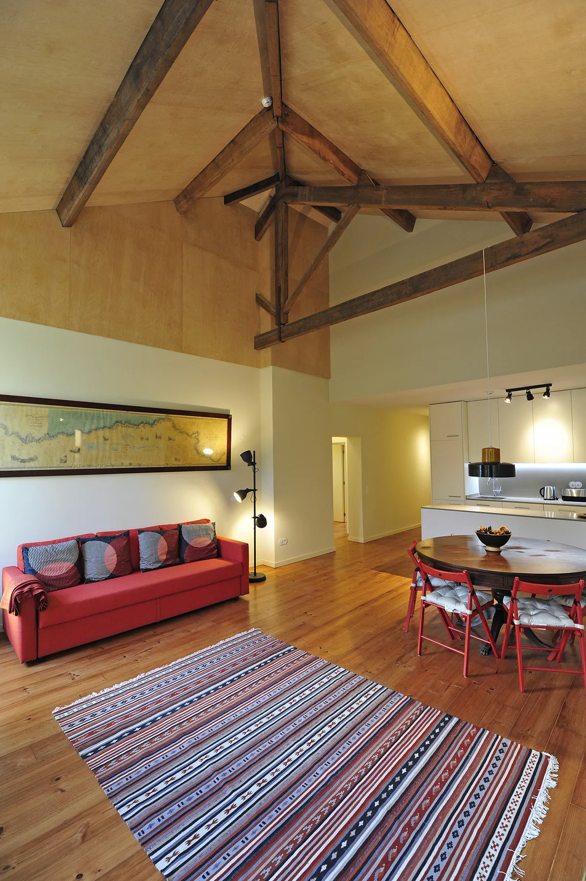Zona de estar y comedor con sofá rojo, alfombra estampada y vigas de madera a la vista.