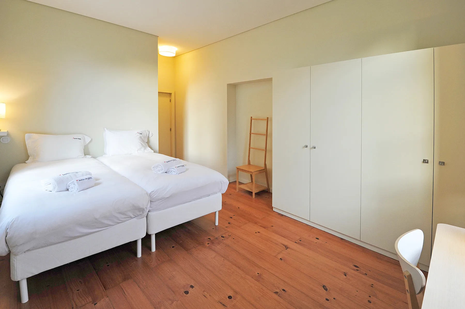 Un dormitorio con dos camas, ropa de cama blanca y suelo de madera.
