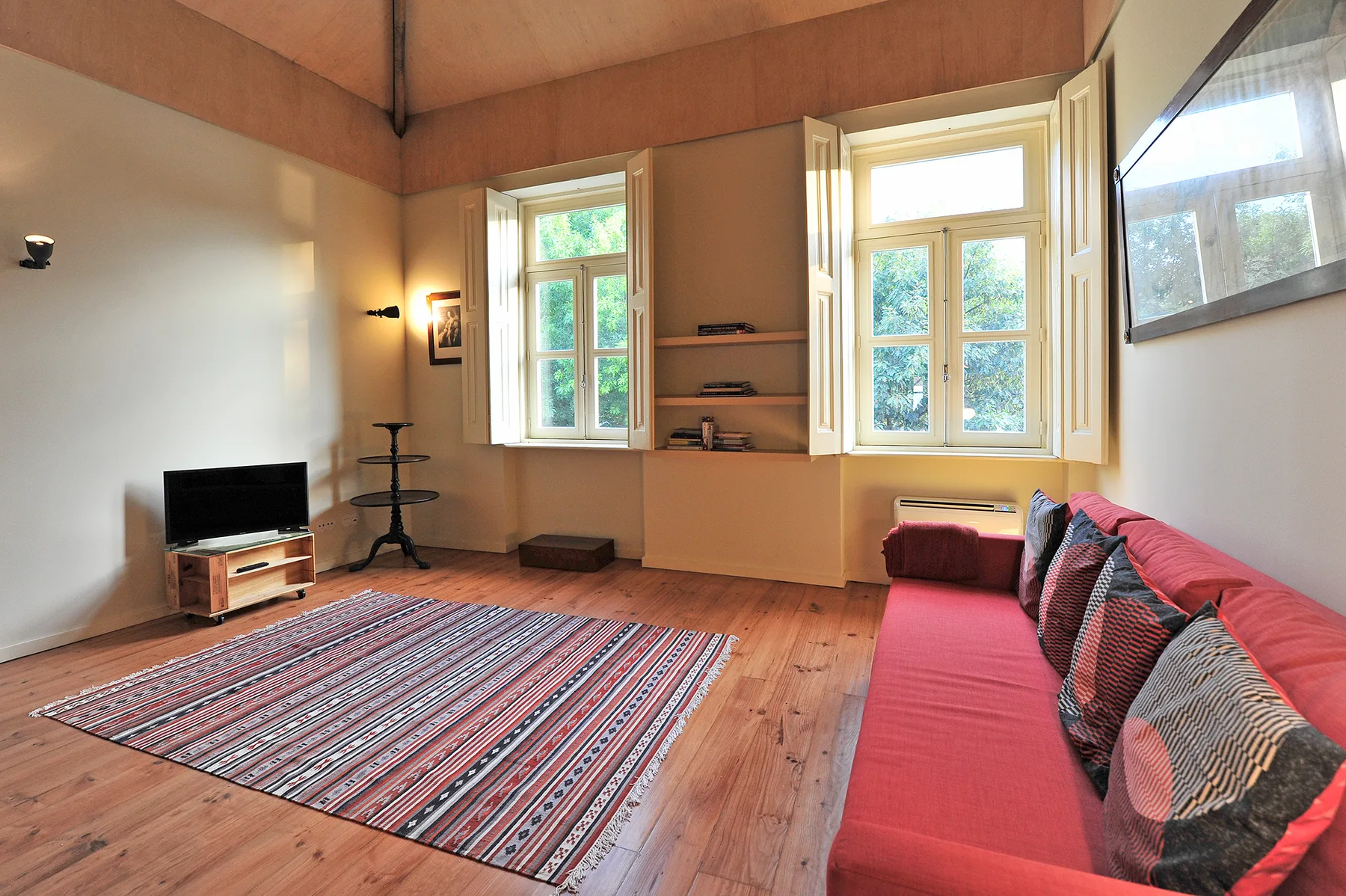 A living room with red seating, a patterned rug, and tall windows.