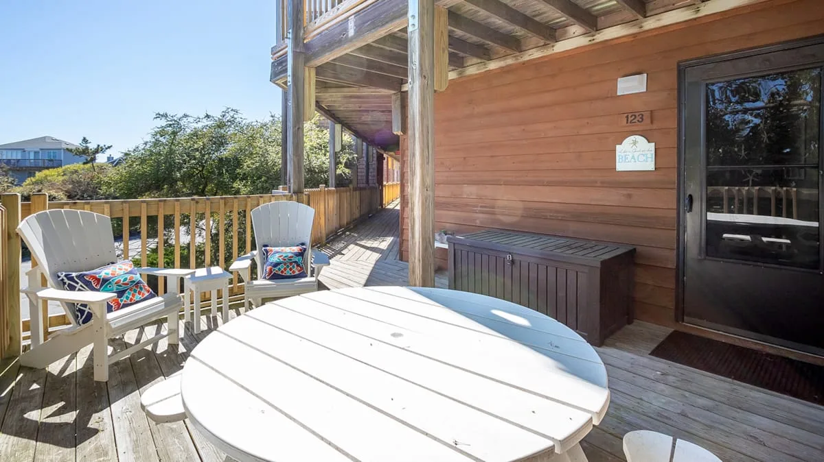 A wooden deck with outdoor seating and a round table beside a cabin.