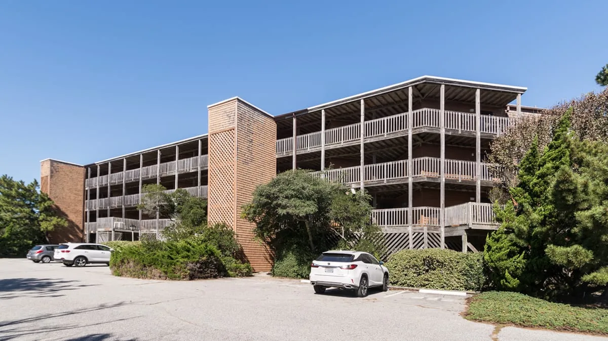 A multi-level parking structure stands beside a paved parking area and greenery.