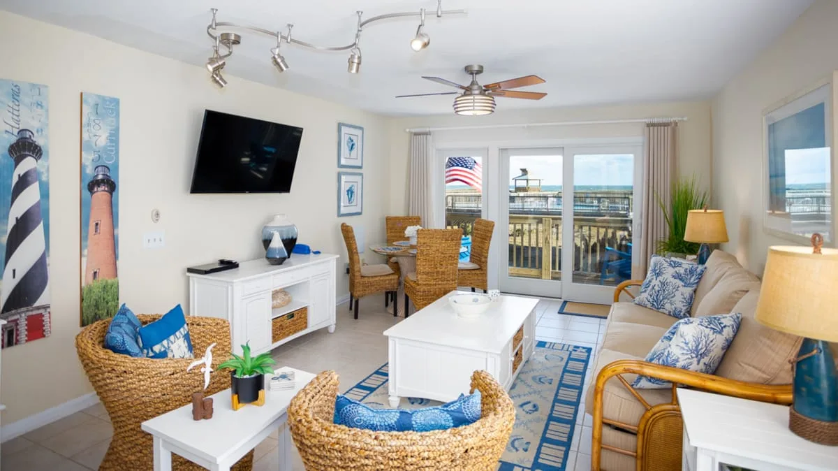 A bright living room with seating, a dining table, and glass doors opening onto a balcony.