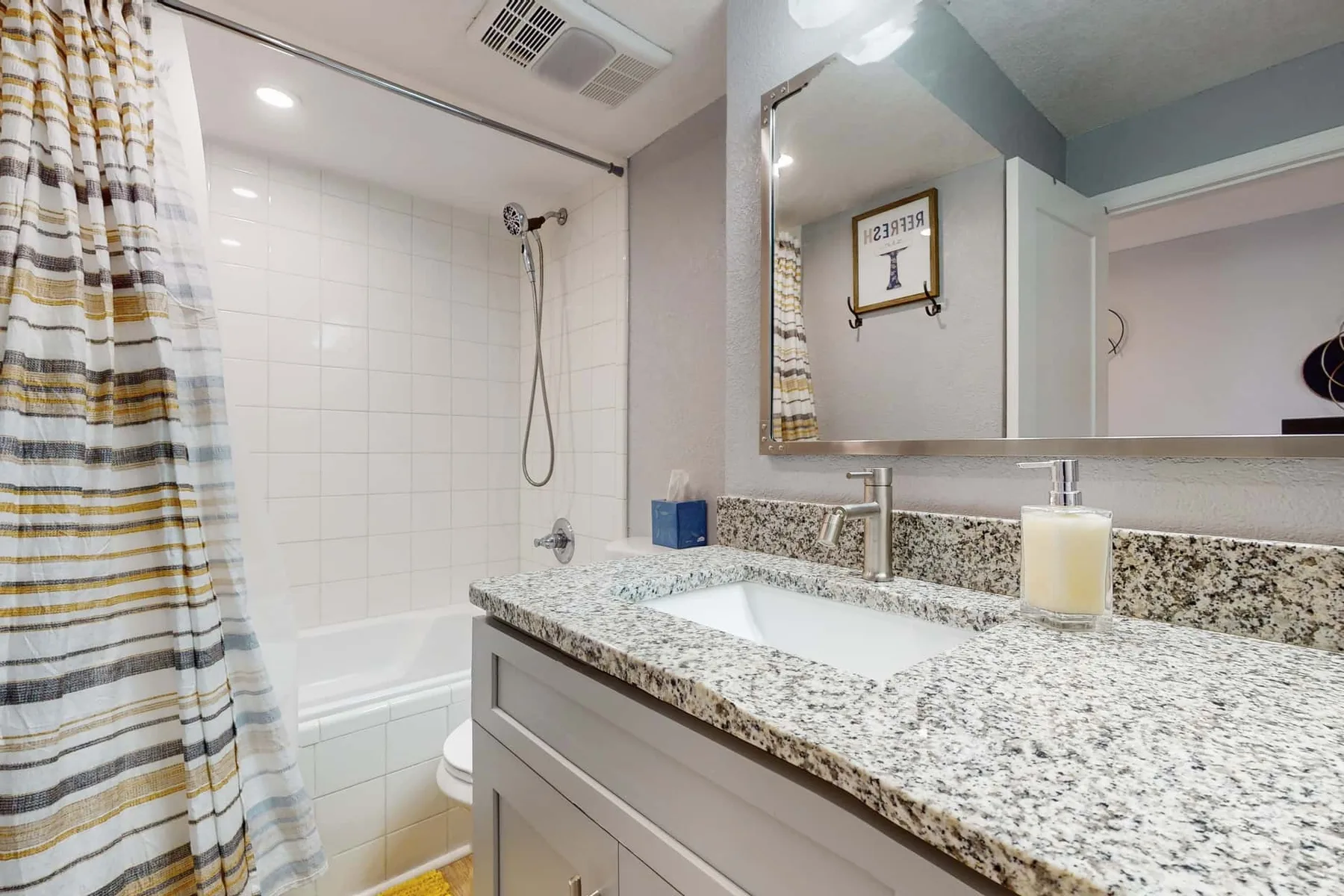 Un baño con bañera, ducha y encimera de tocador con aspecto de granito.