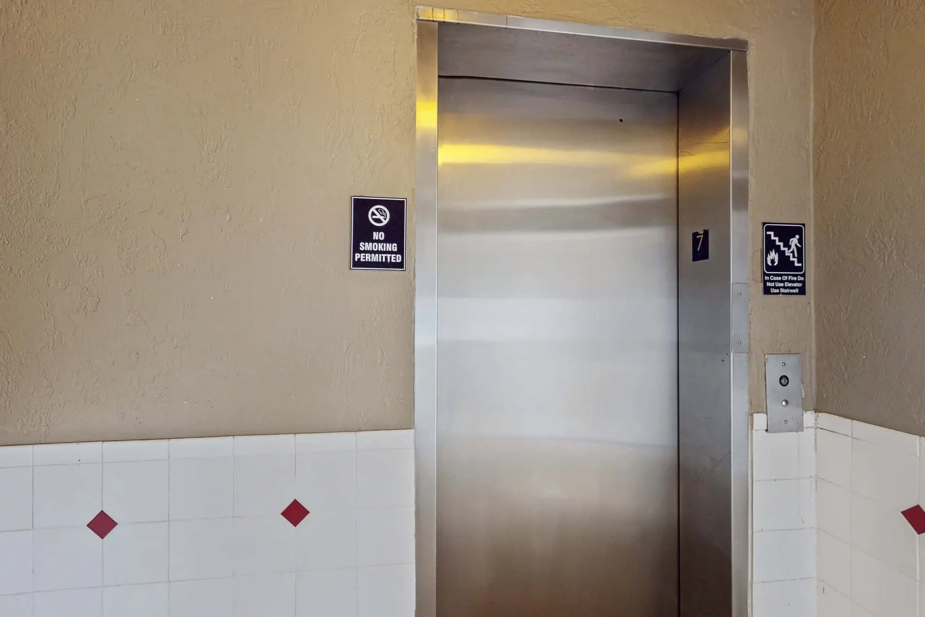Un ascensor con las puertas metálicas cerradas está empotrado en una pared alicatada.