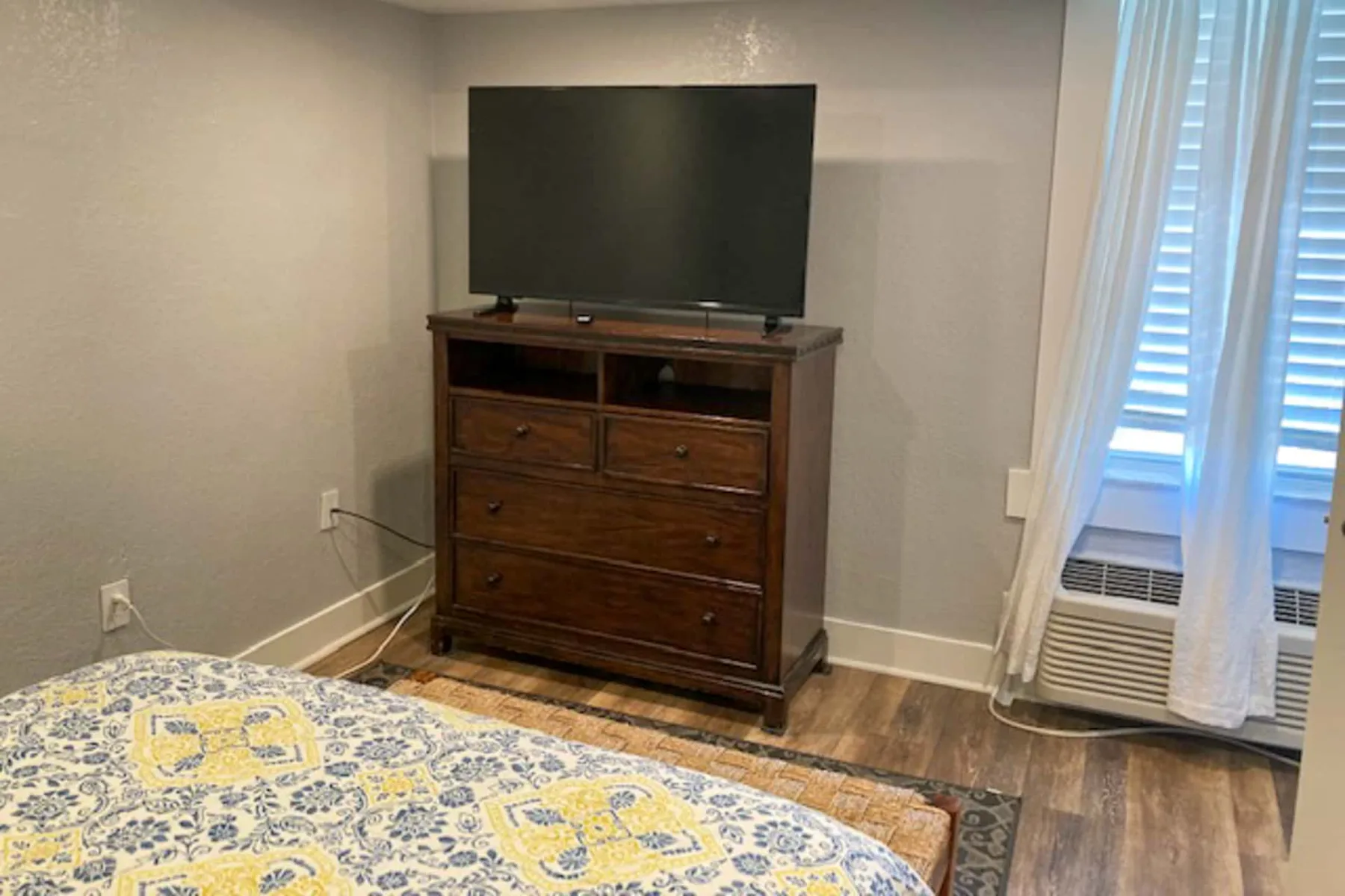 Un dormitorio con un televisor sobre una cómoda de madera junto a una ventana.