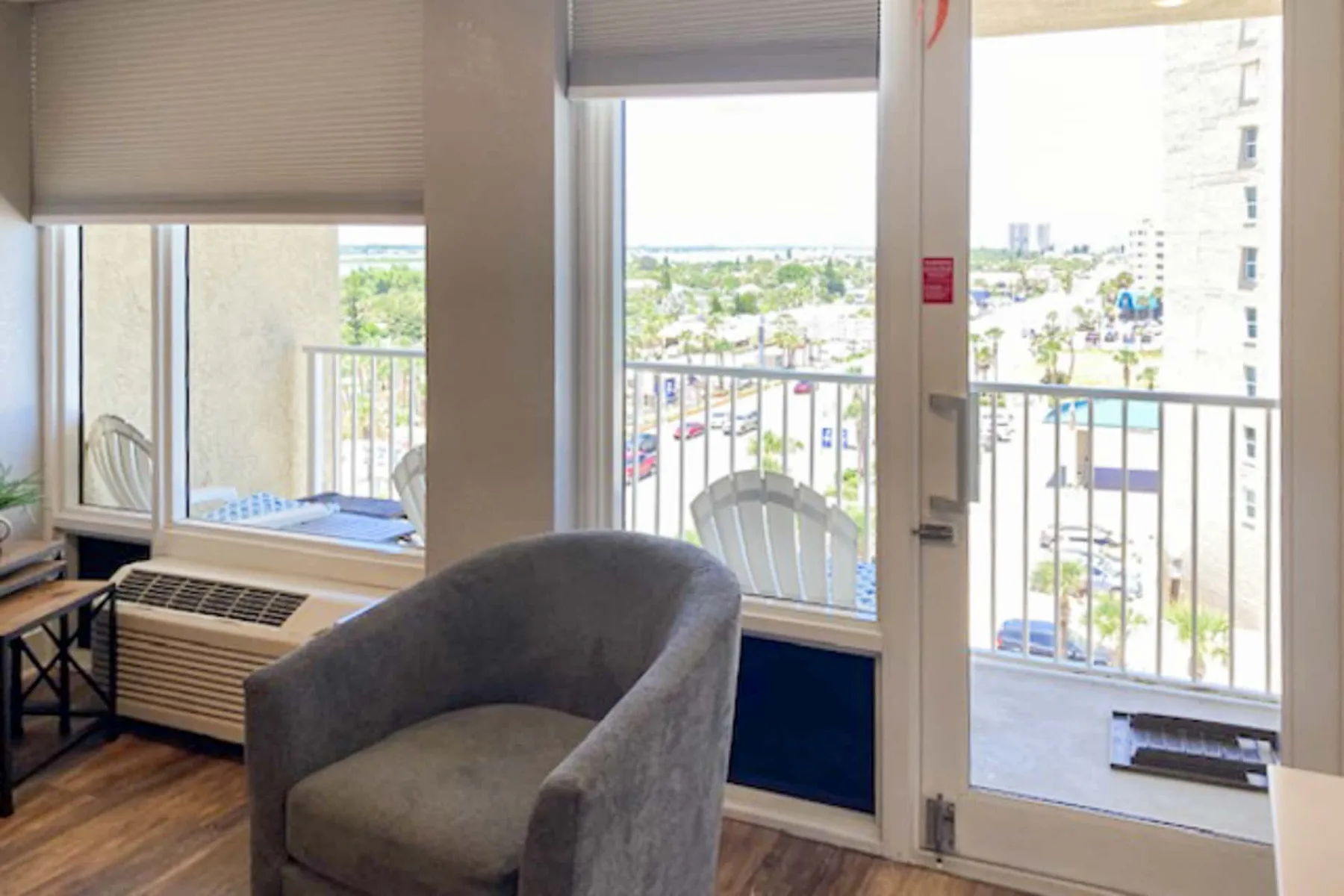 Una luminosa zona de estar con un sillón junto a grandes ventanas que dan a un balcón.