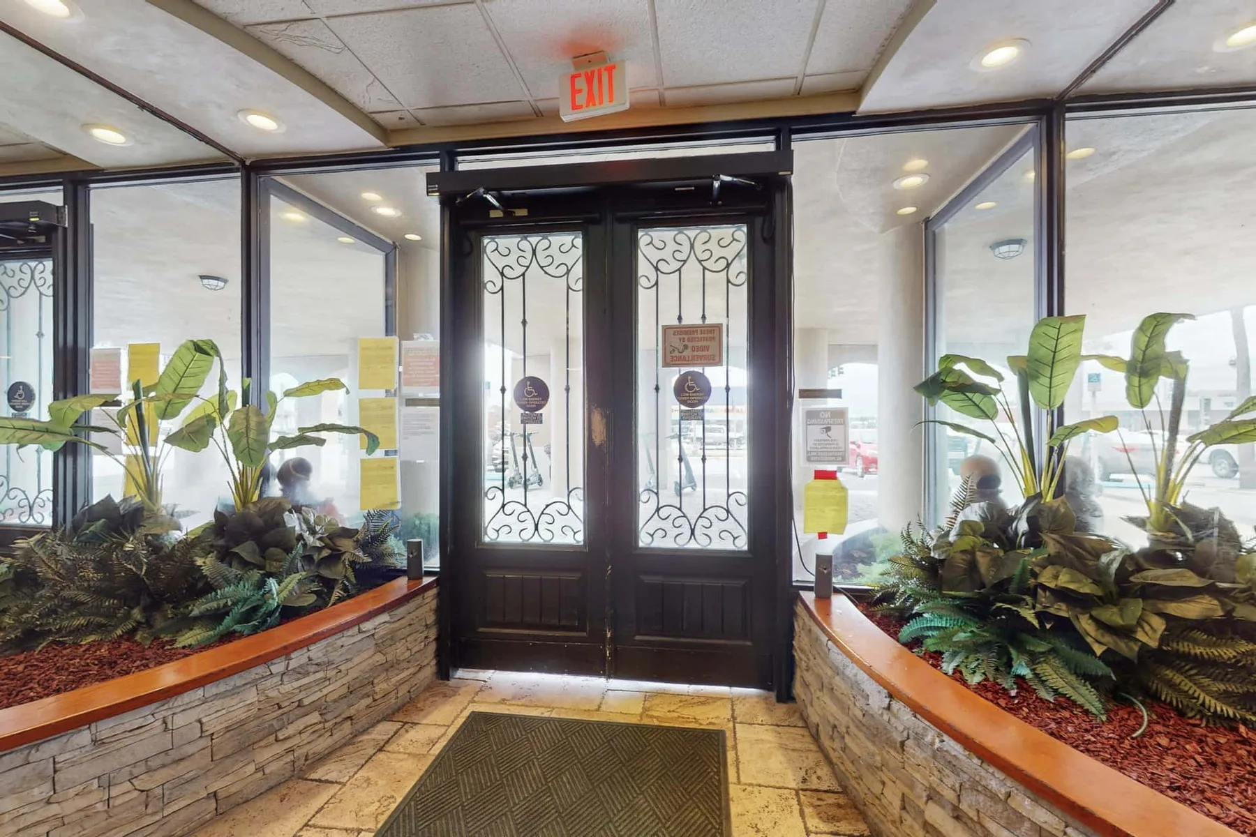 Un vestíbulo de entrada con puertas dobles oscuras y jardineras elevadas a ambos lados.