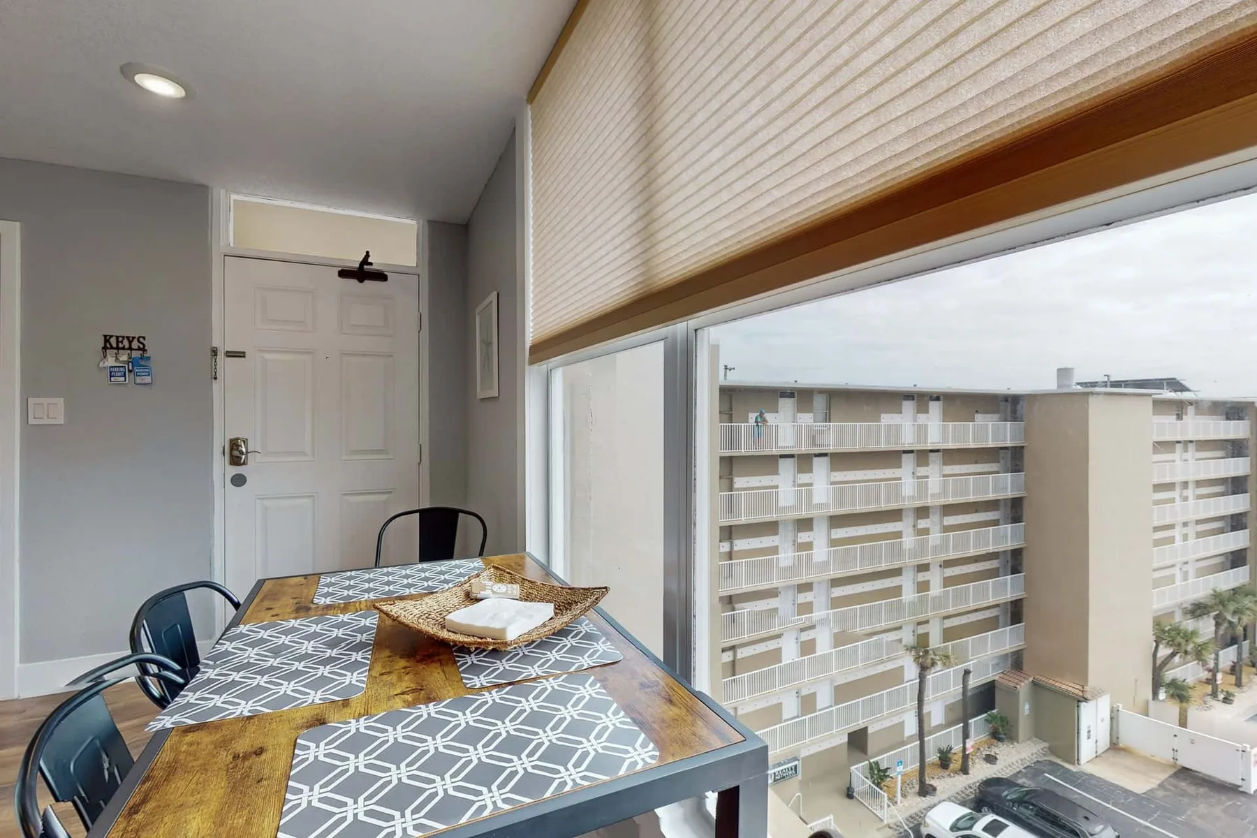 Comedor con una mesa junto a grandes ventanas con vistas a edificios cercanos.