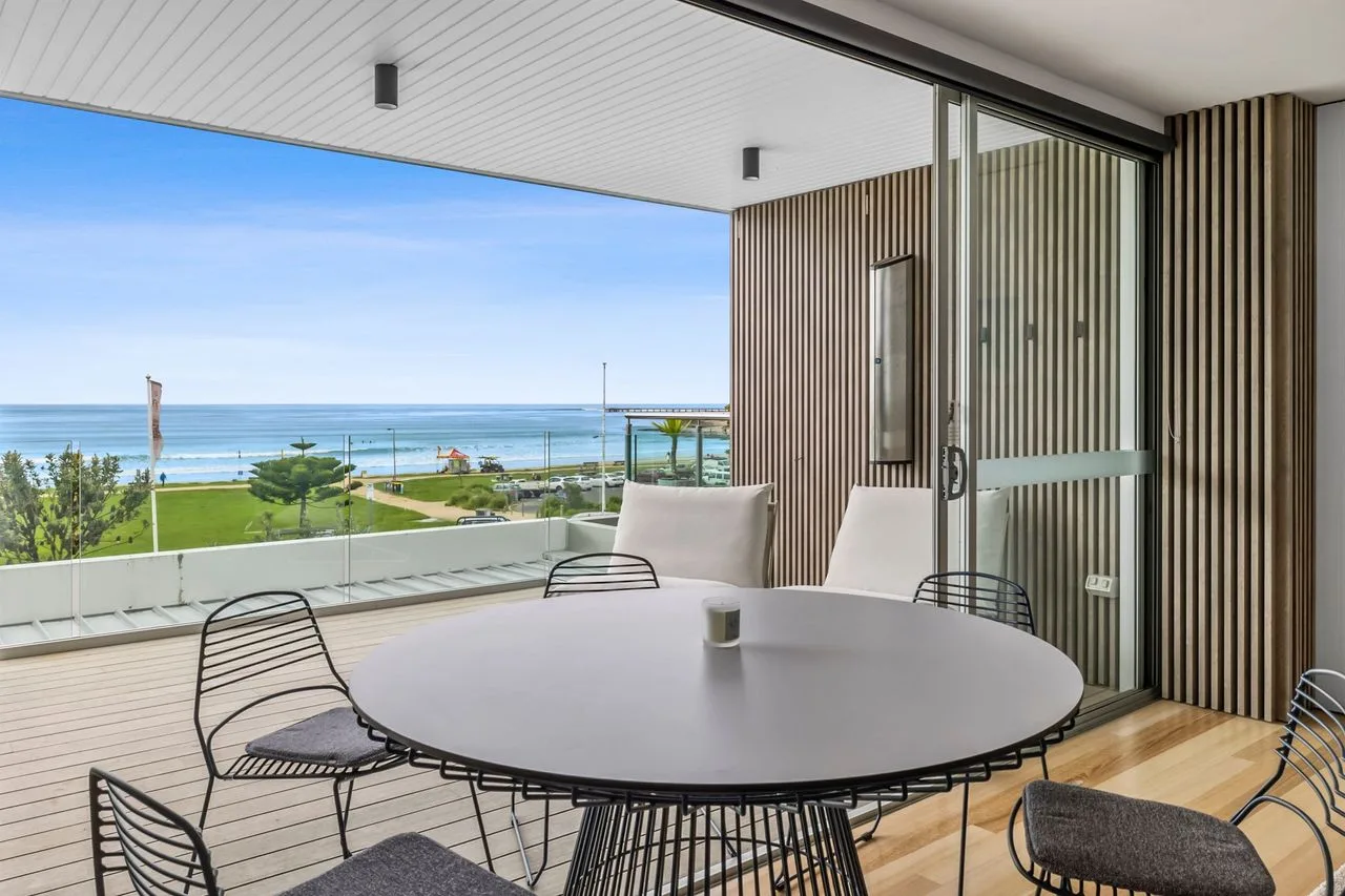 A covered outdoor dining area overlooks the ocean and a green lawn.