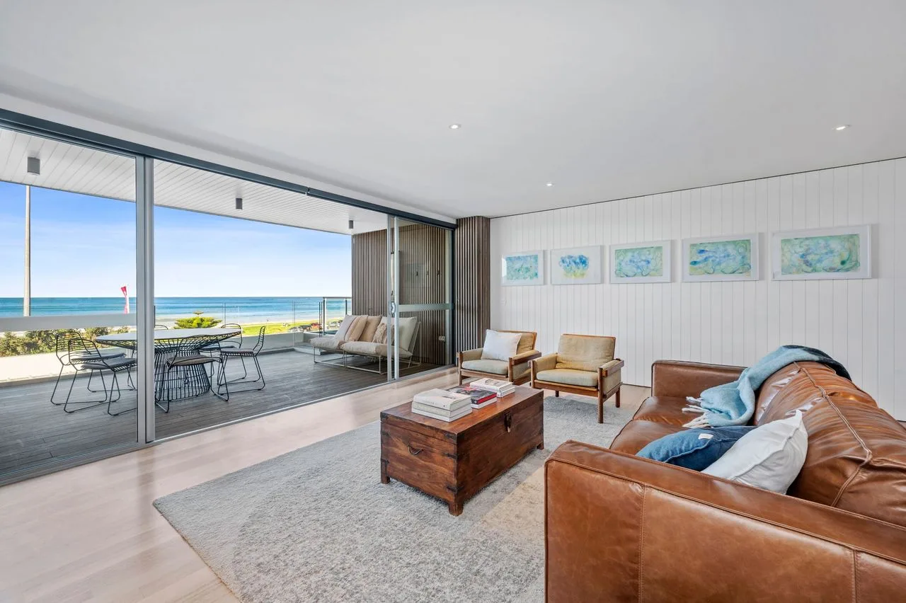 Una sala luminosa se abre a un balcón con vistas al mar.